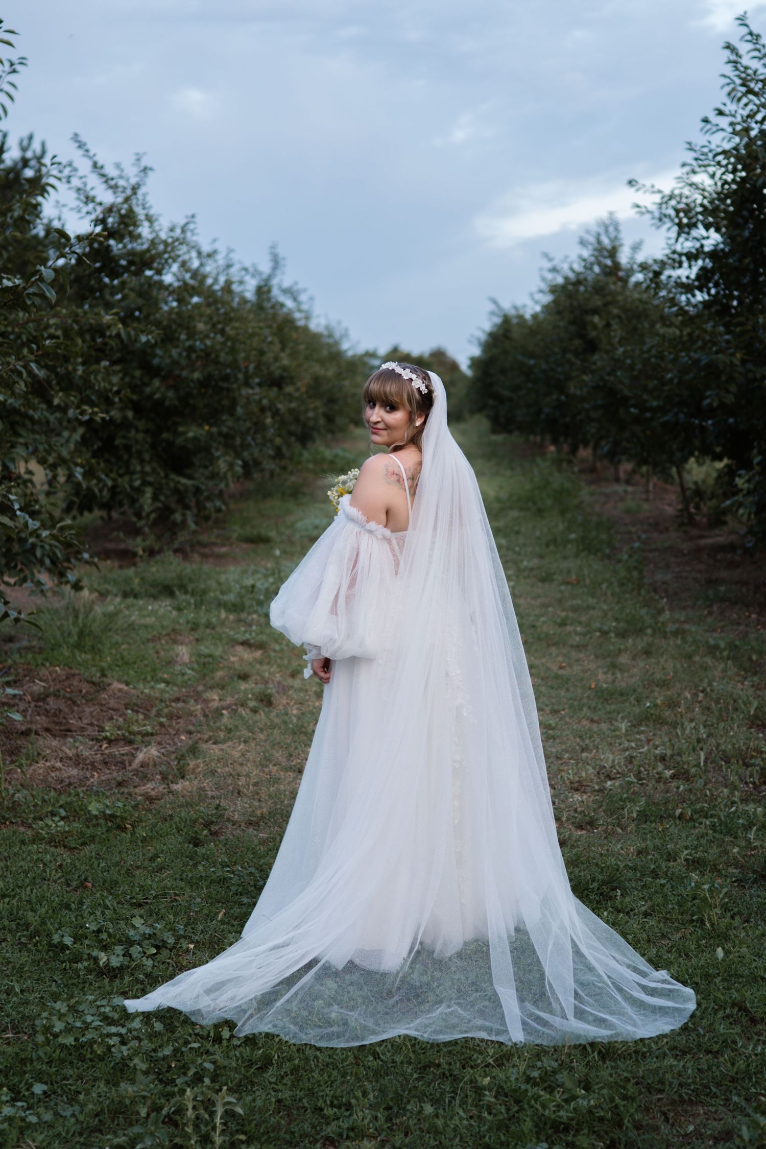 A flowing white wedding dress and veil photographed in an orchard setting.