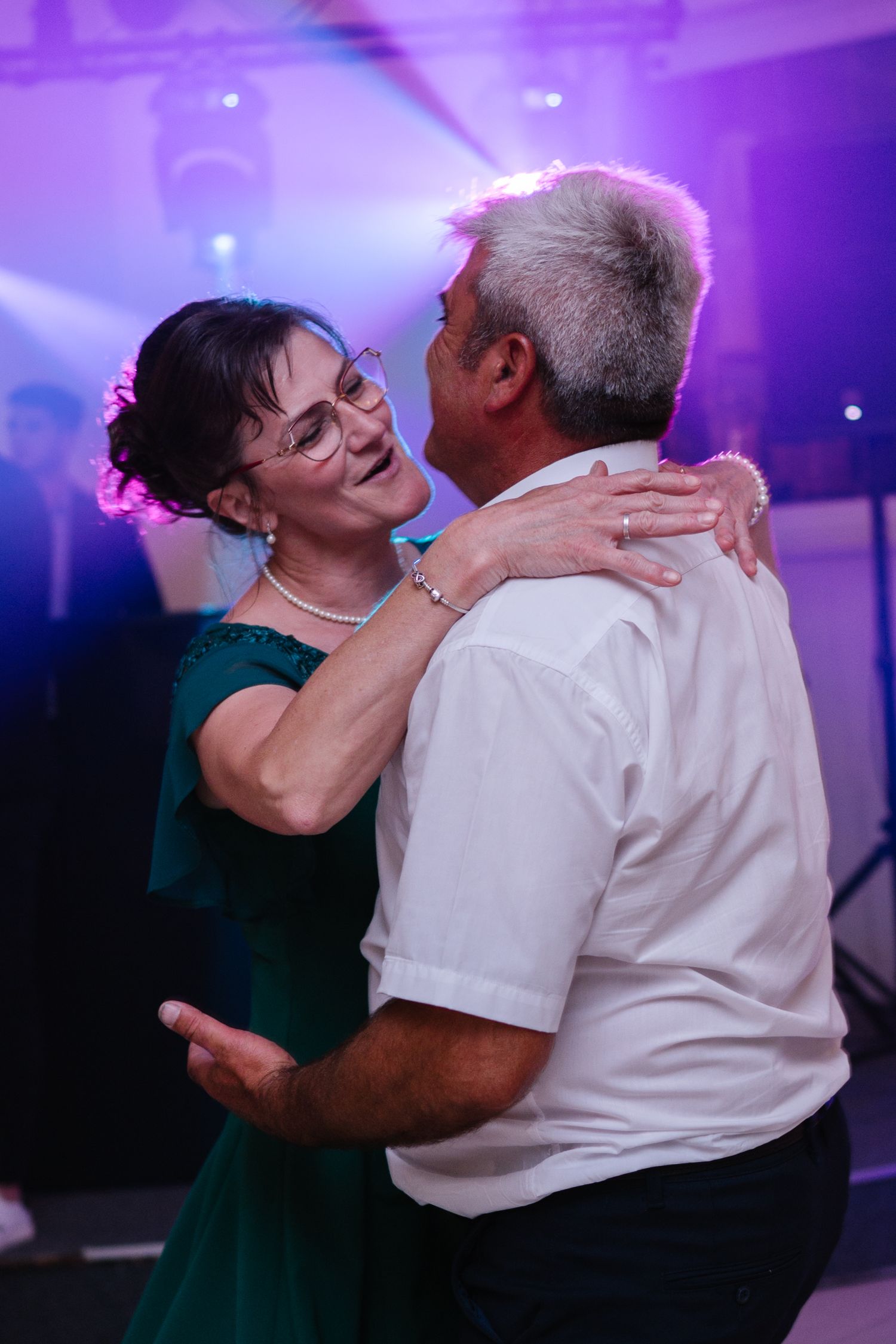 Wedding guests share emotional dance under purple lighting during evening reception.