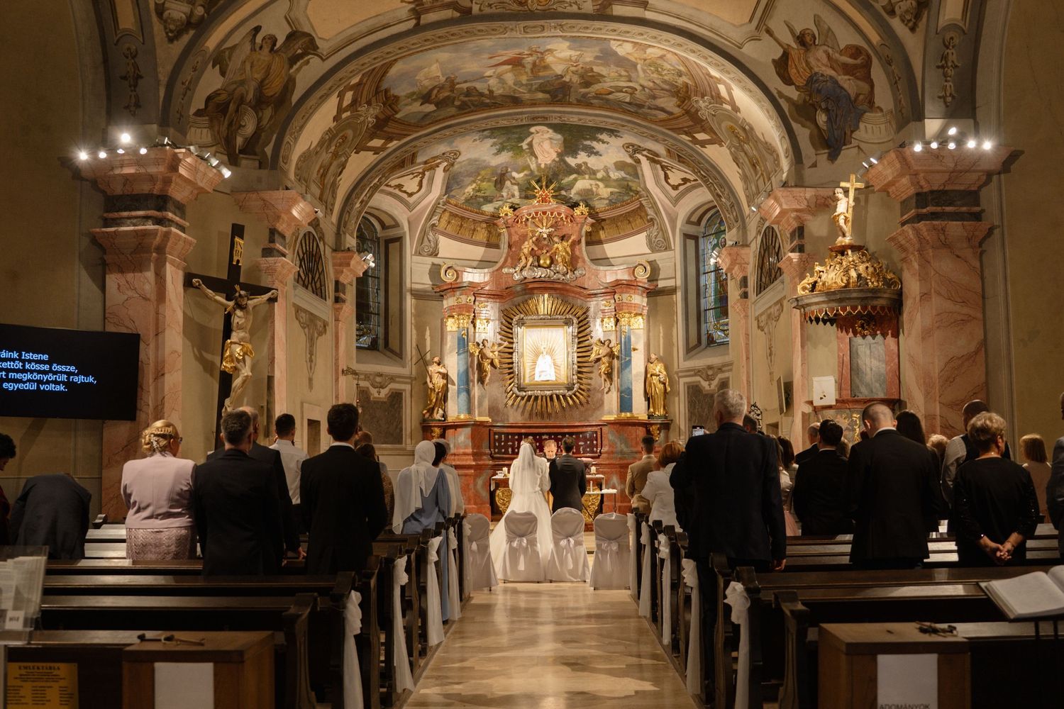 Interior of an ornate Catholic church during a wedding ceremony with guests seated in wooden pews.