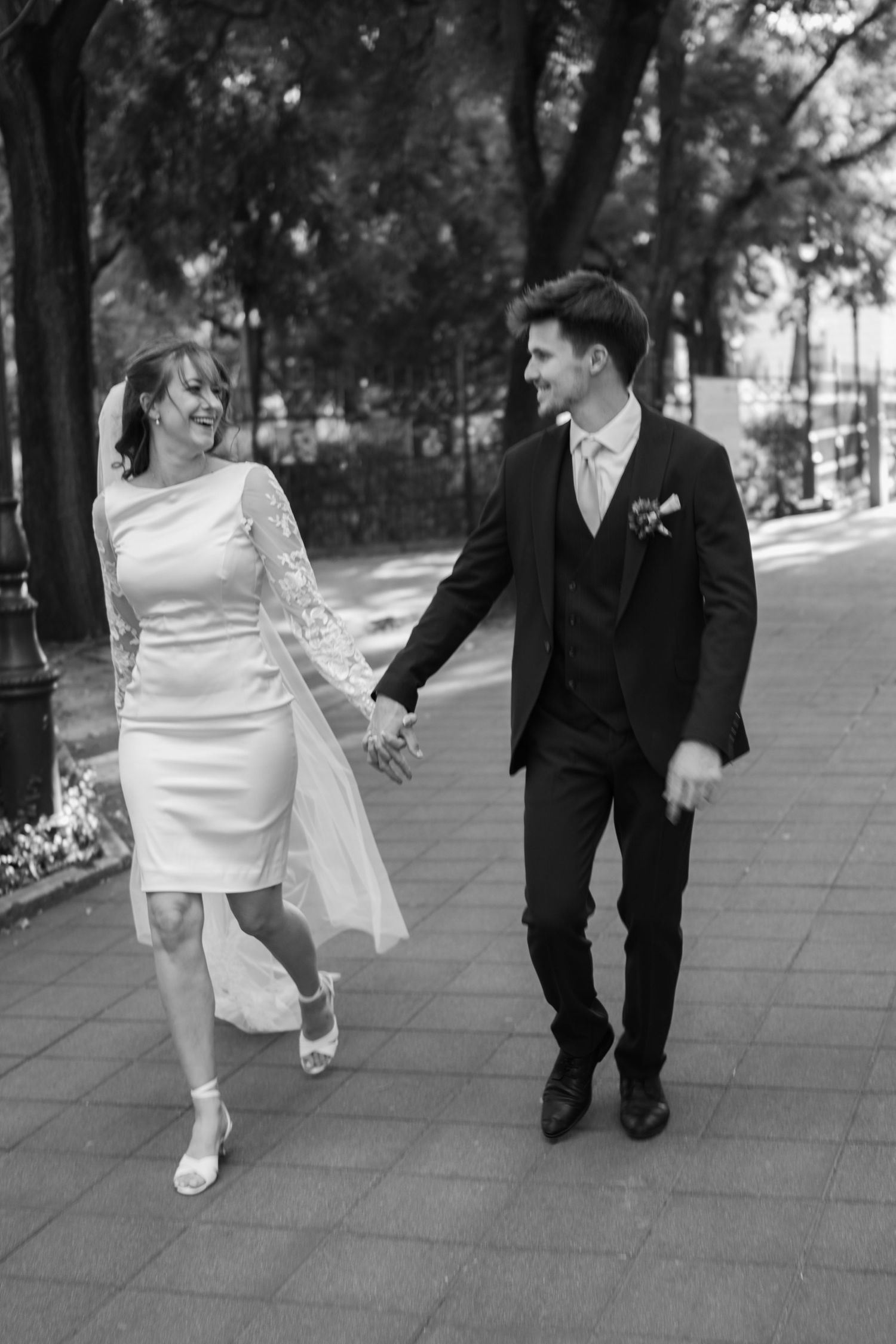 Black and white photo of newlyweds walking together on a paved pathway.