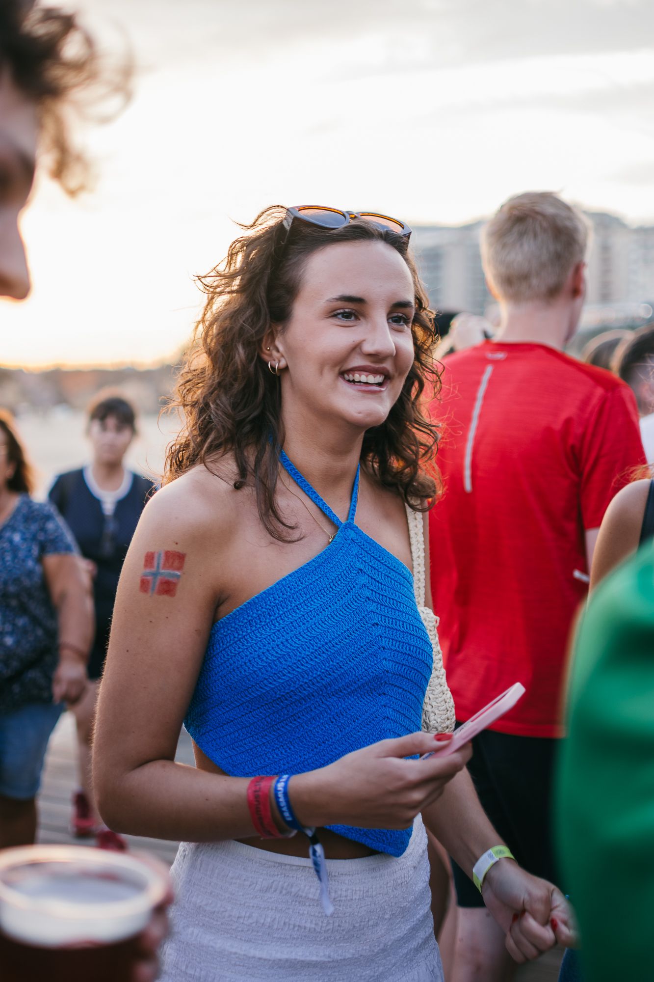 A person in a bright blue top smiling and enjoying an outdoor event at sunset.