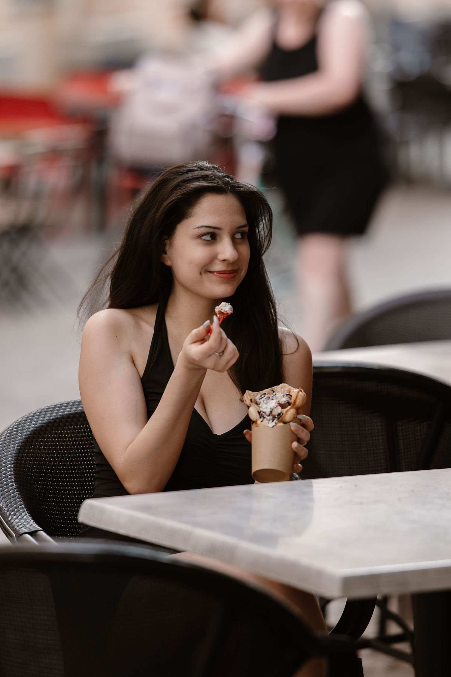 Woman enjoying a relaxing moment at an outdoor cafe table with dark decor and natural lighting.