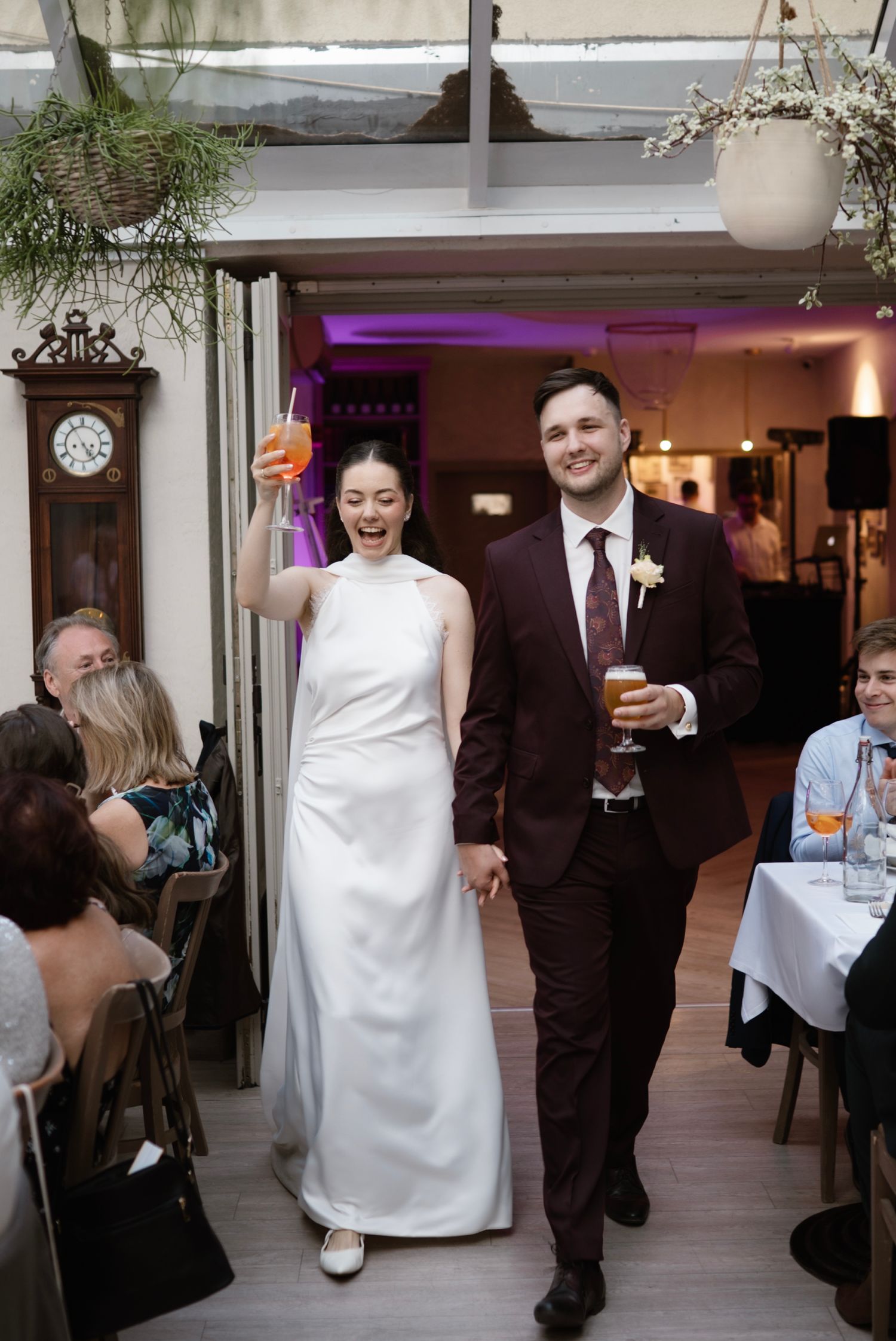 Newlyweds making grand entrance holding drinks at indoor wedding reception venue.