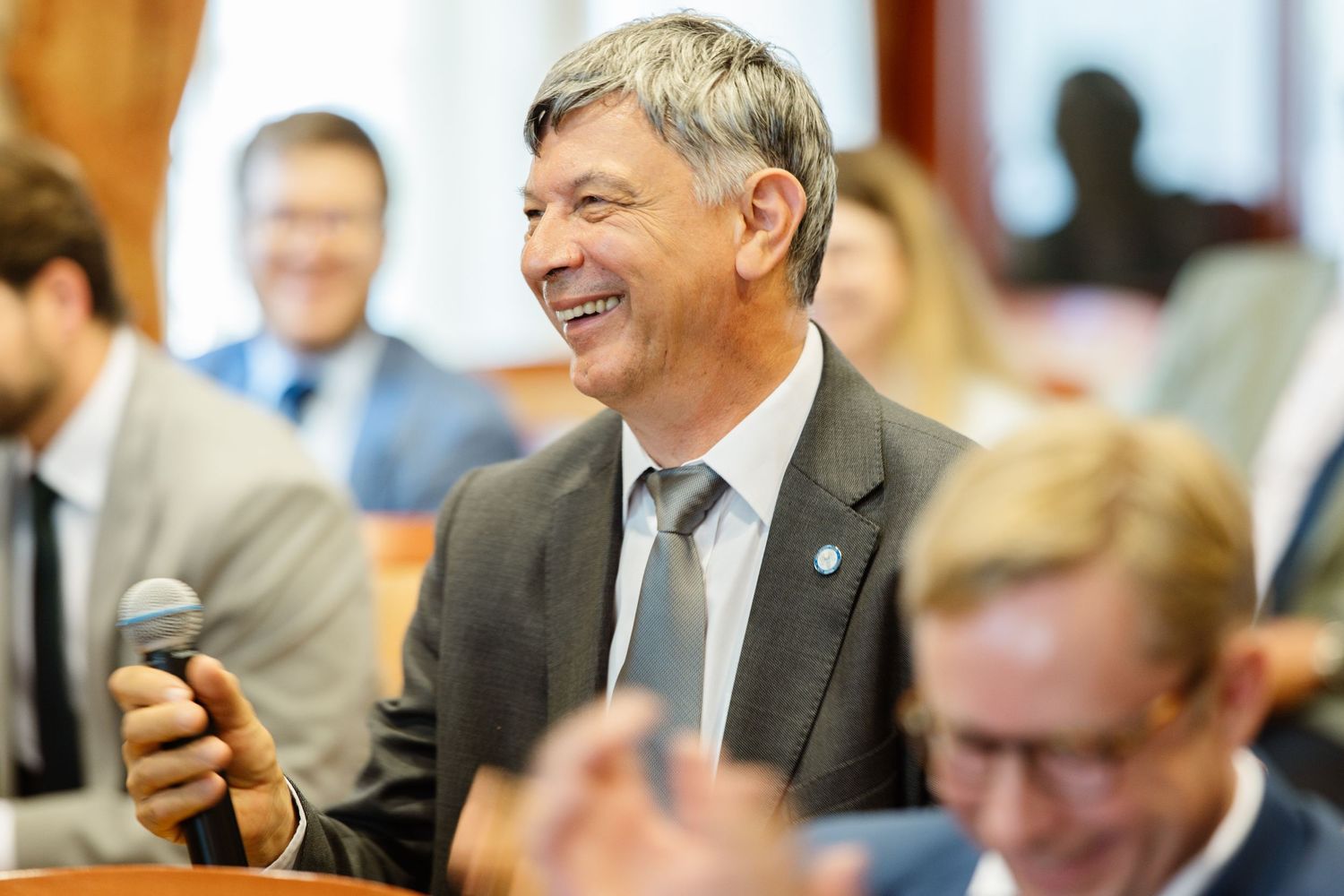 A group of people in business attire sit at a conference table, smiling and engaged in conversation.