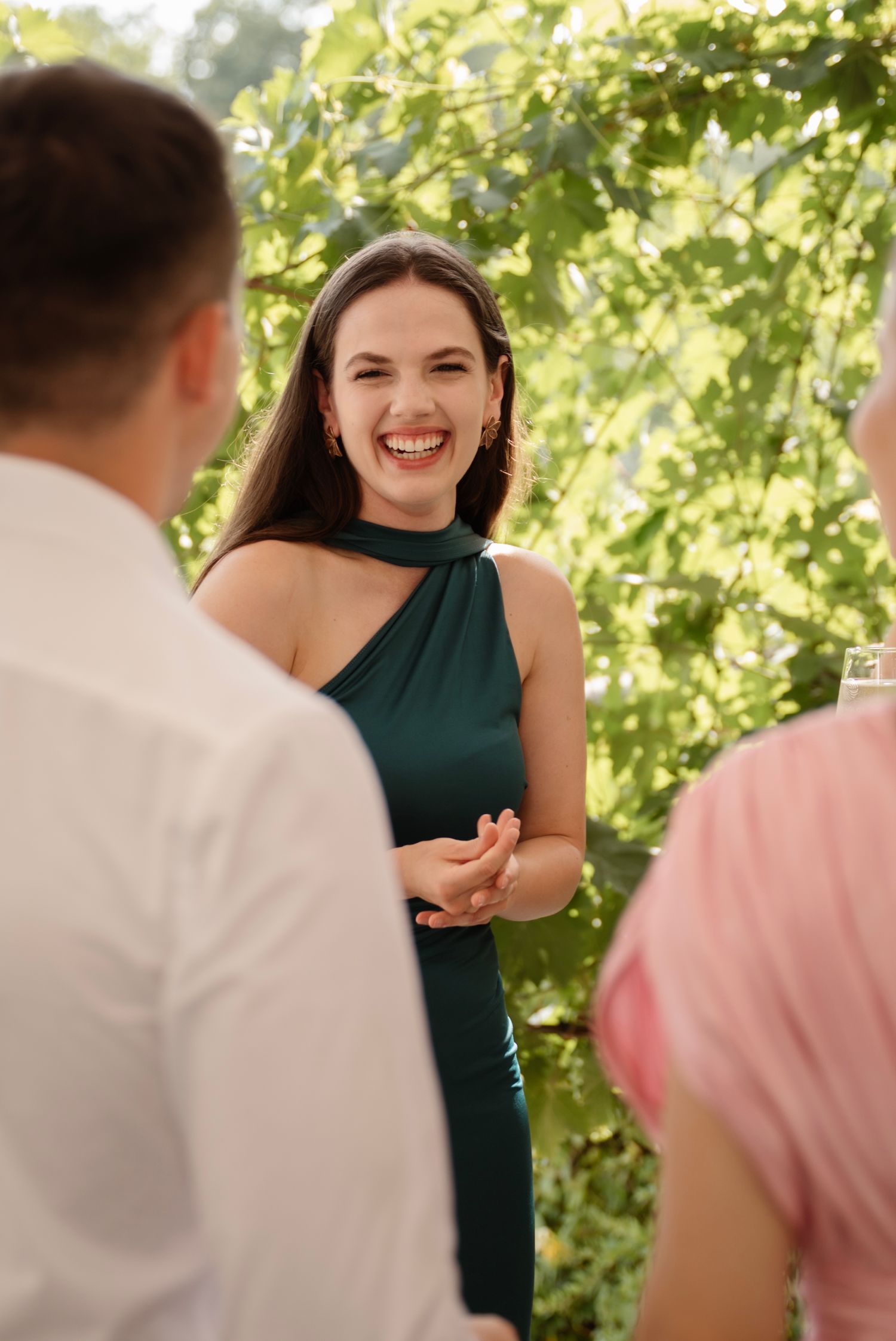 A smiling woman in a green dress enjoys an outdoor garden party conversation with guests.