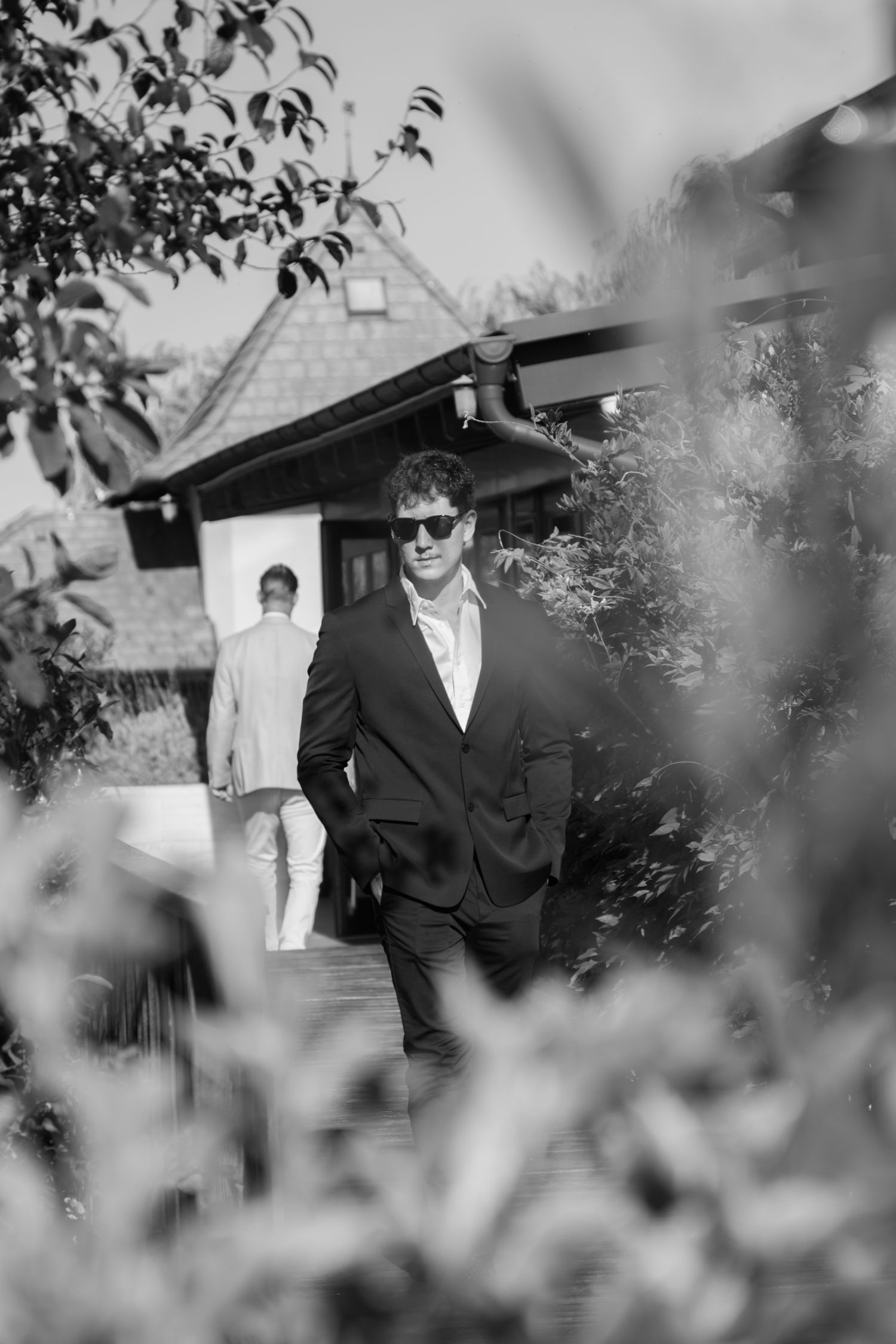 Stylish groomsmen in suits and sunglasses photographed through foliage.