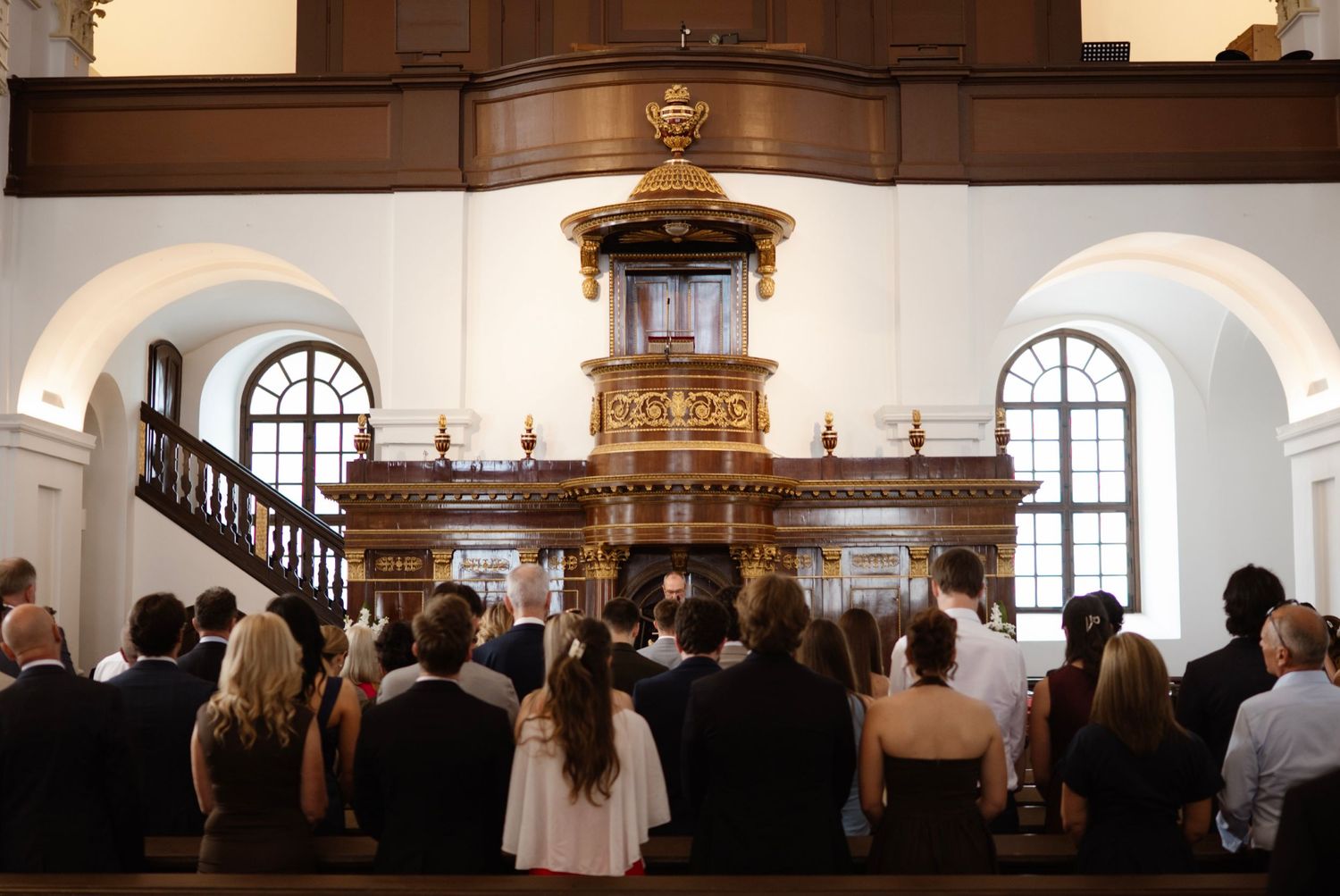 Wedding guests seated in ornate church pews facing a golden baroque altar during a formal ceremony.