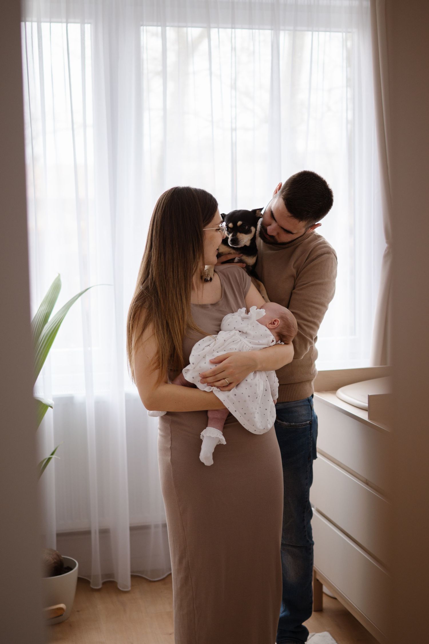 A tender family moment captured in a series of intimate photographs by a window with soft natural light streaming in.