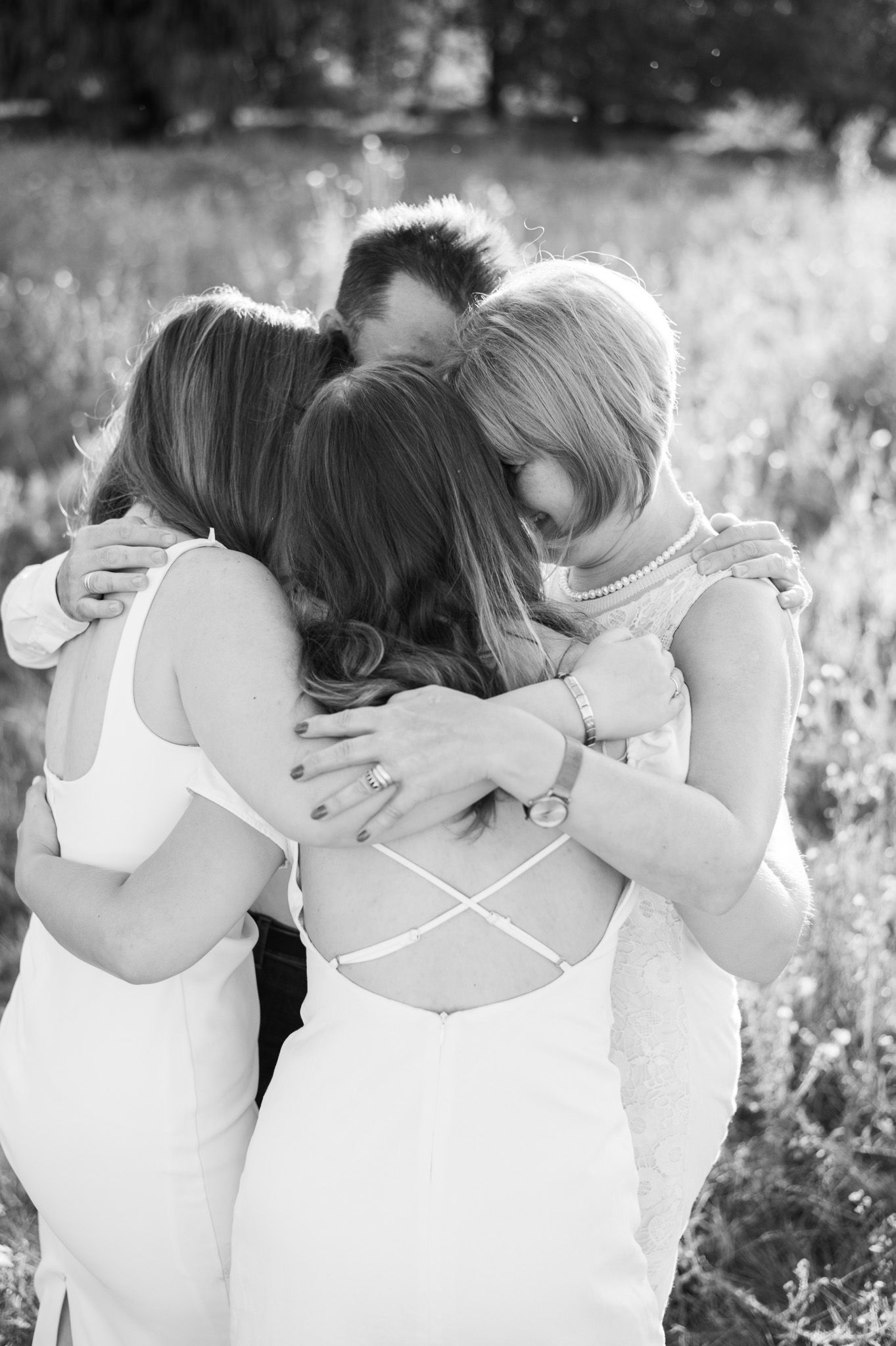 Friends in white outfits embracing each other in a field during a black and white photoshoot.
