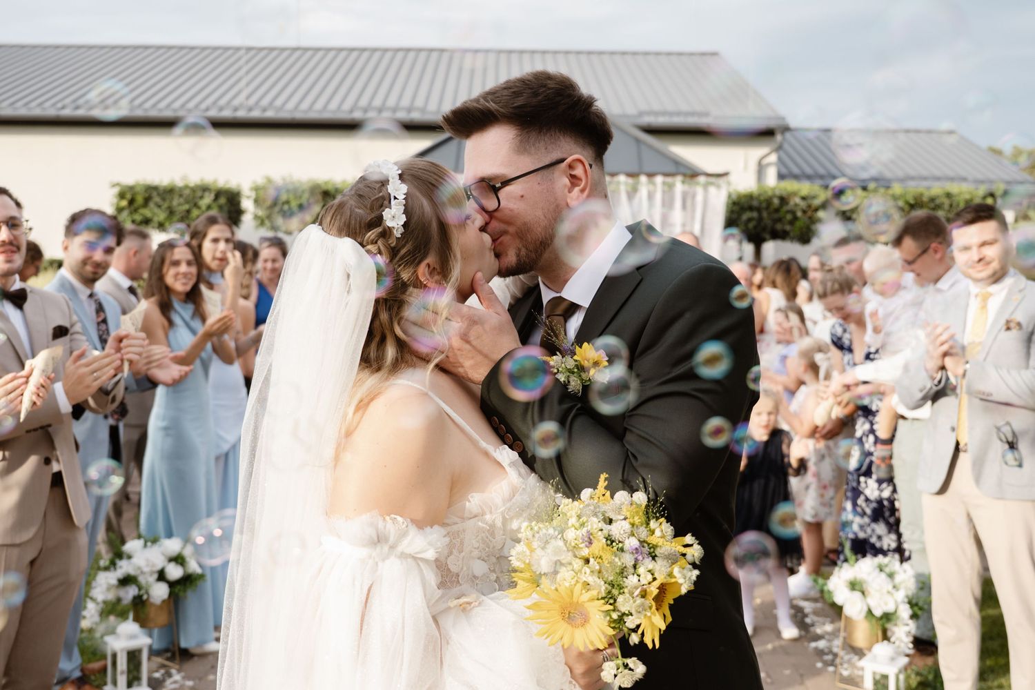 A wedding couple shares a joyful moment surrounded by yellow sunflowers and guests.