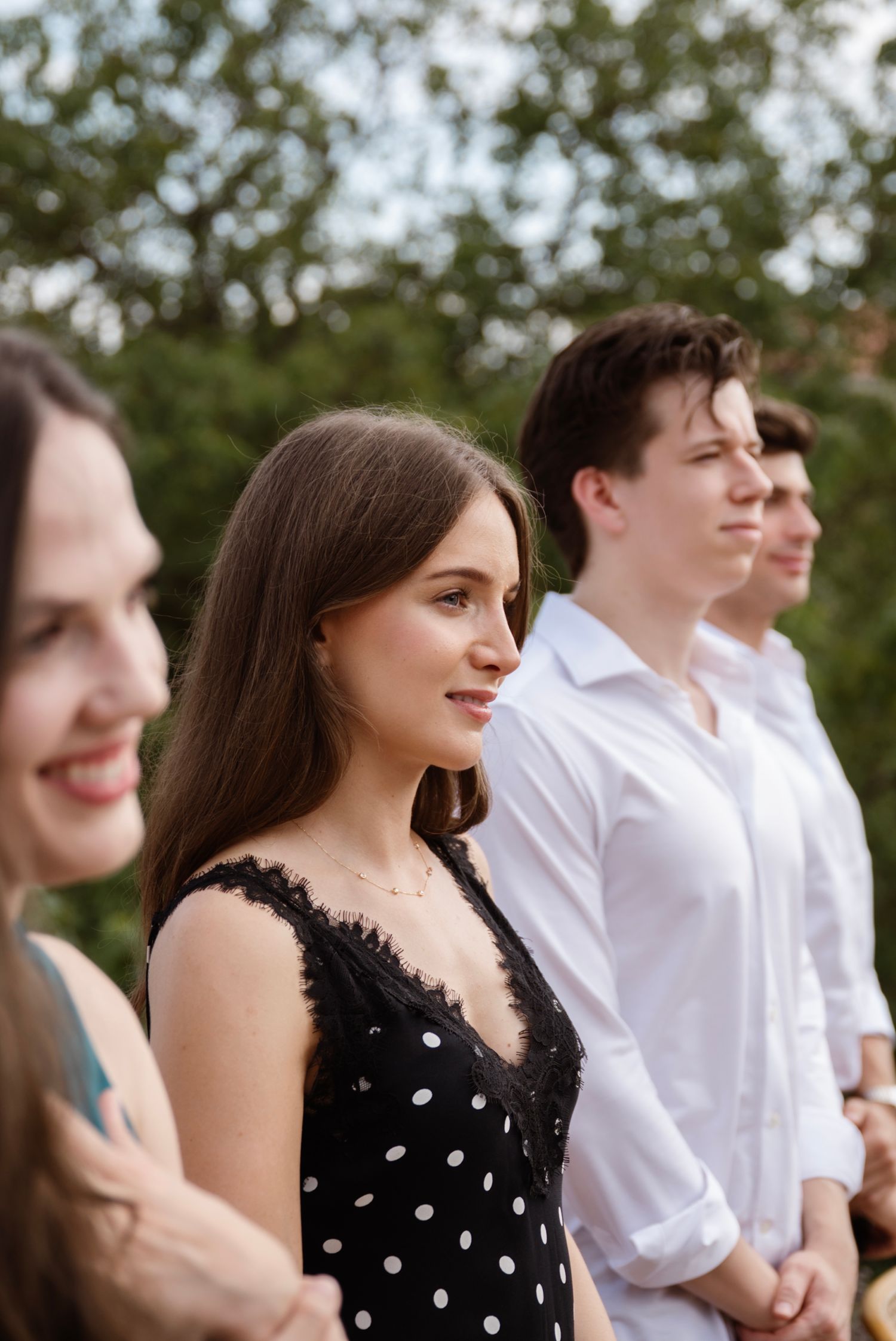 Young guests in elegant attire standing outdoors at a summer wedding celebration.