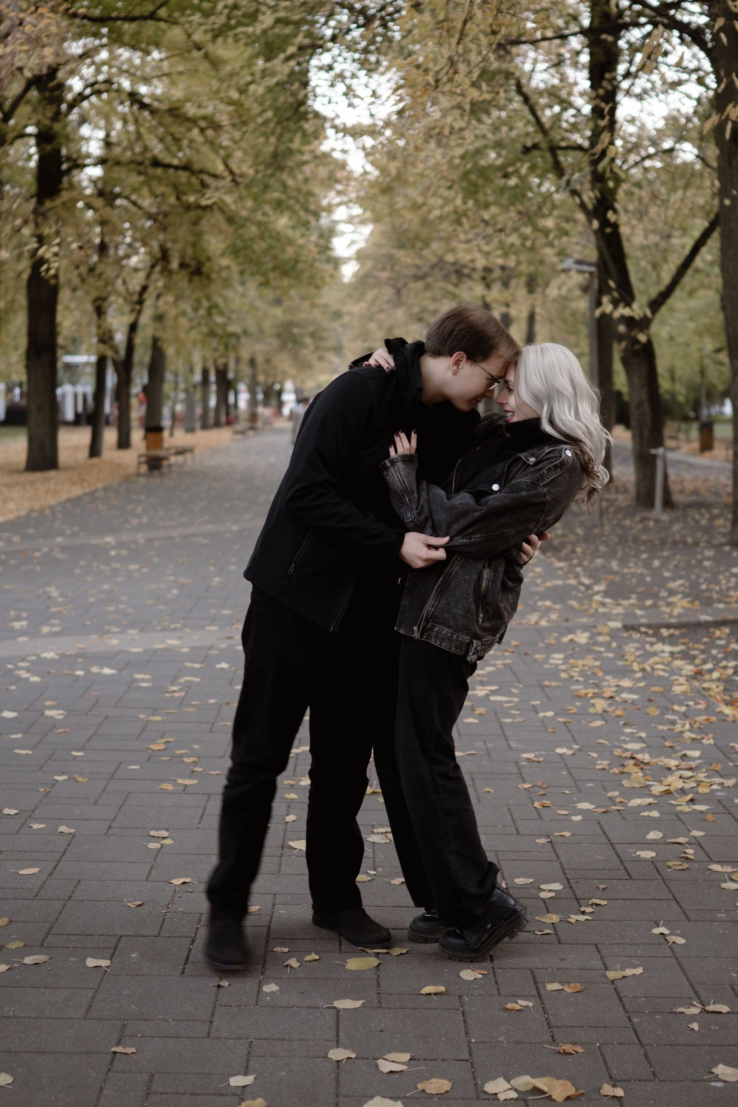 Couple in matching dark outfits sharing playful moment on autumn path.