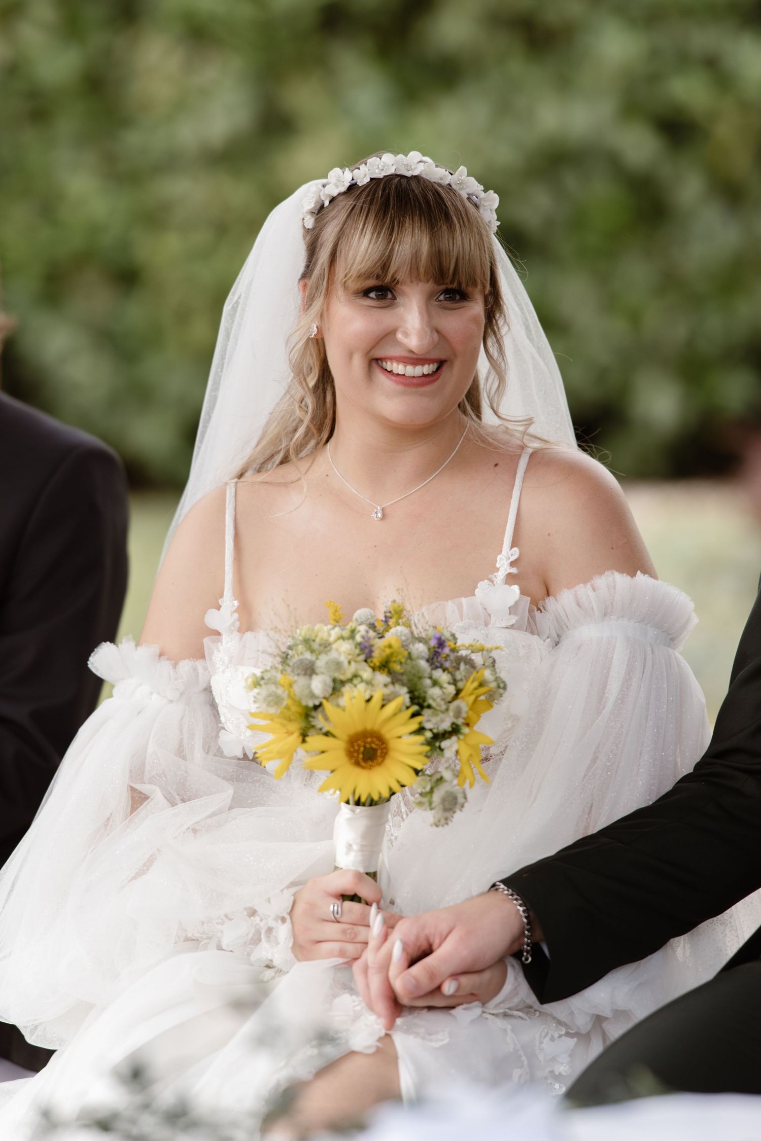 Bride holding a vibrant yellow sunflower bouquet in a white off-shoulder wedding dress.