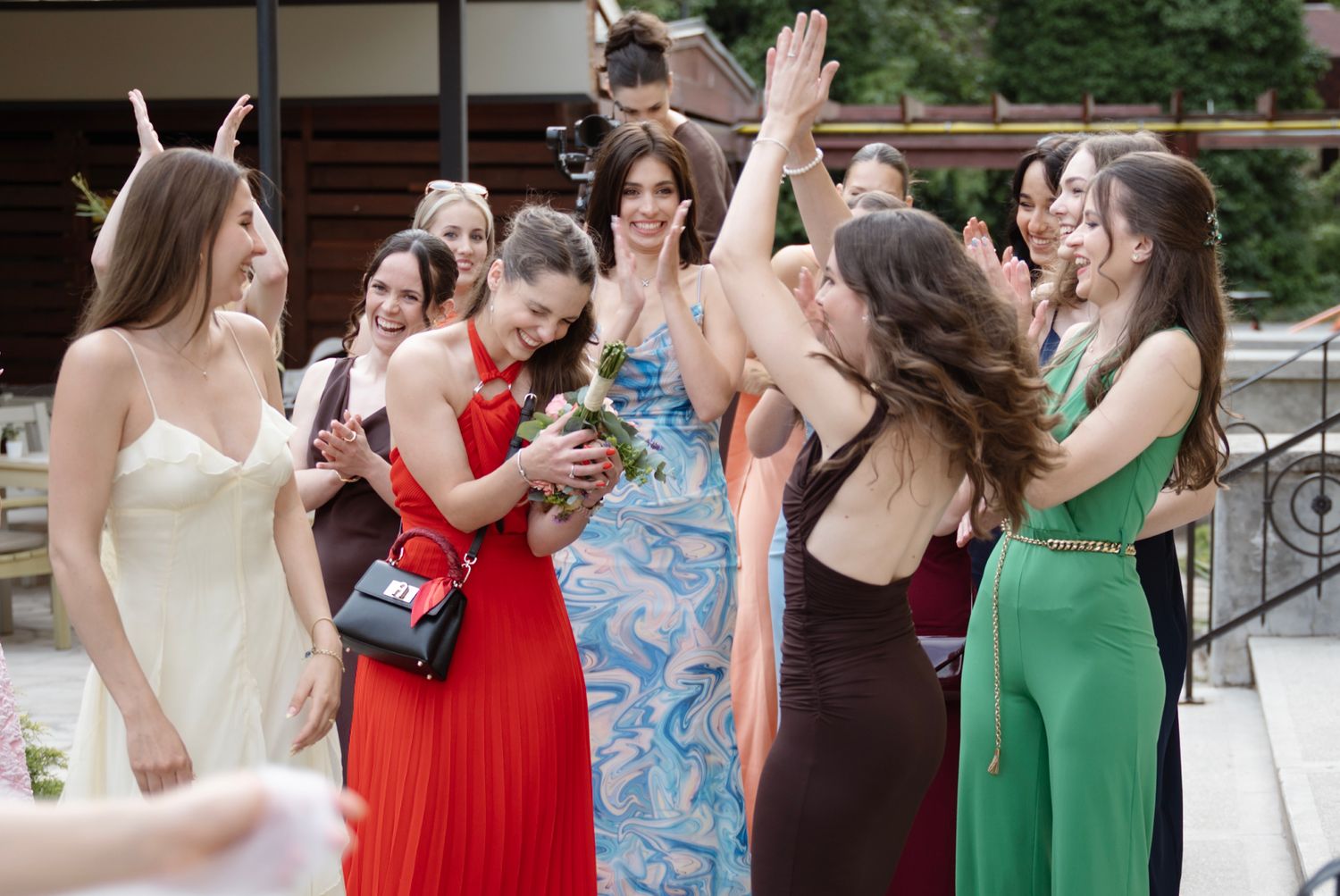 Group of elegantly dressed women in colorful gowns celebrating together at a formal outdoor event.