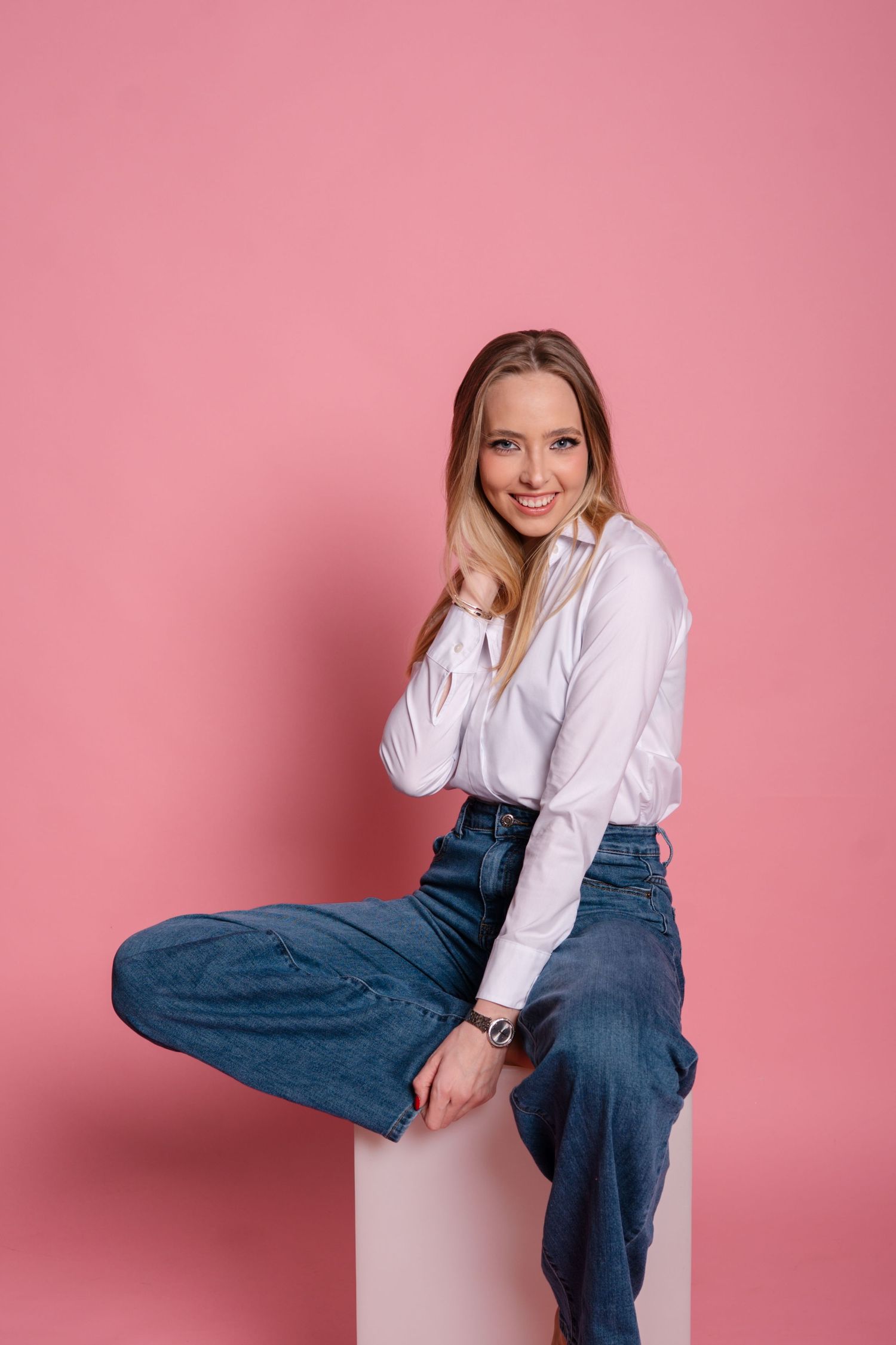 Playful fashion portraits against pink background wearing white shirt and blue jeans.