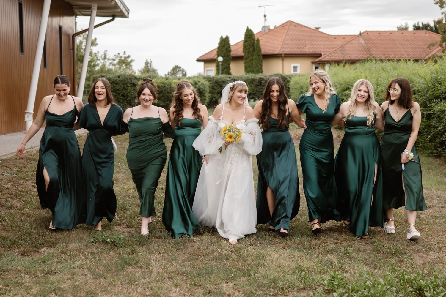 A bridal party in emerald green dresses posing with the bride in white.