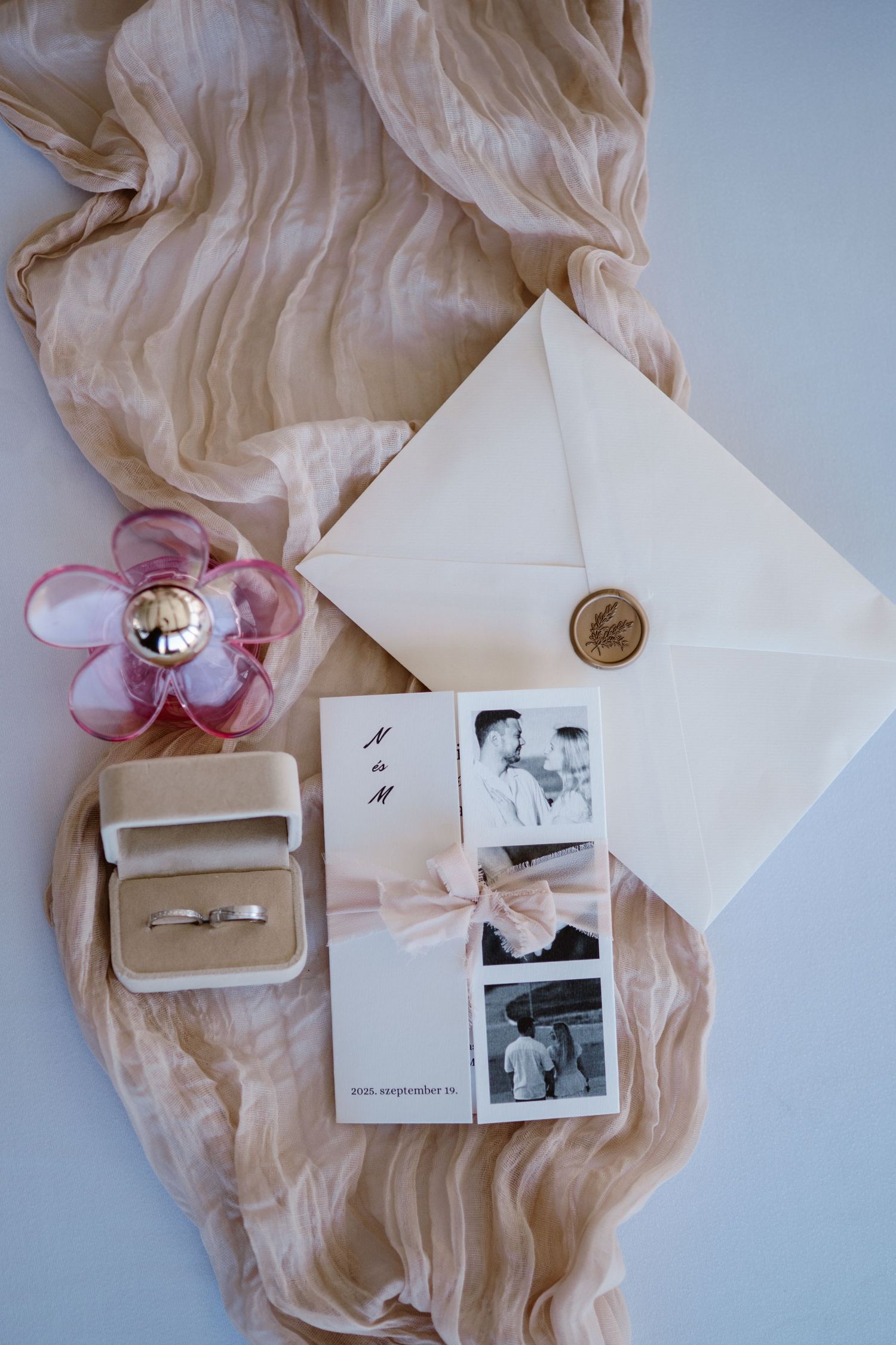 Wedding details flatlay with ring box, photos and delicate blush fabric.