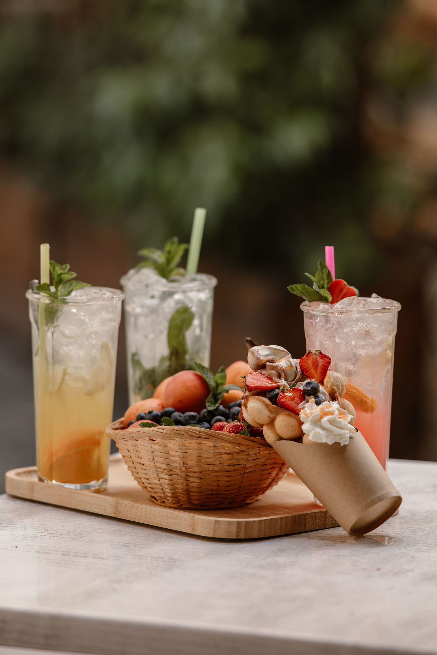 Refreshing summer cocktails garnished with berries and herbs served on marble table with light snacks.