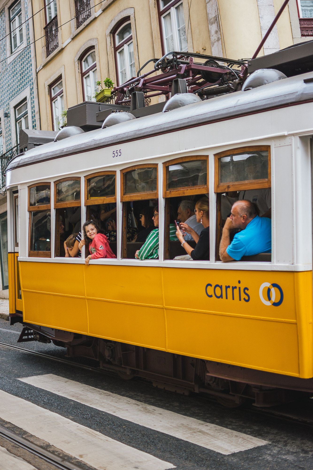 Yellow vintage tram car travels through historic city streets with passengers aboard.