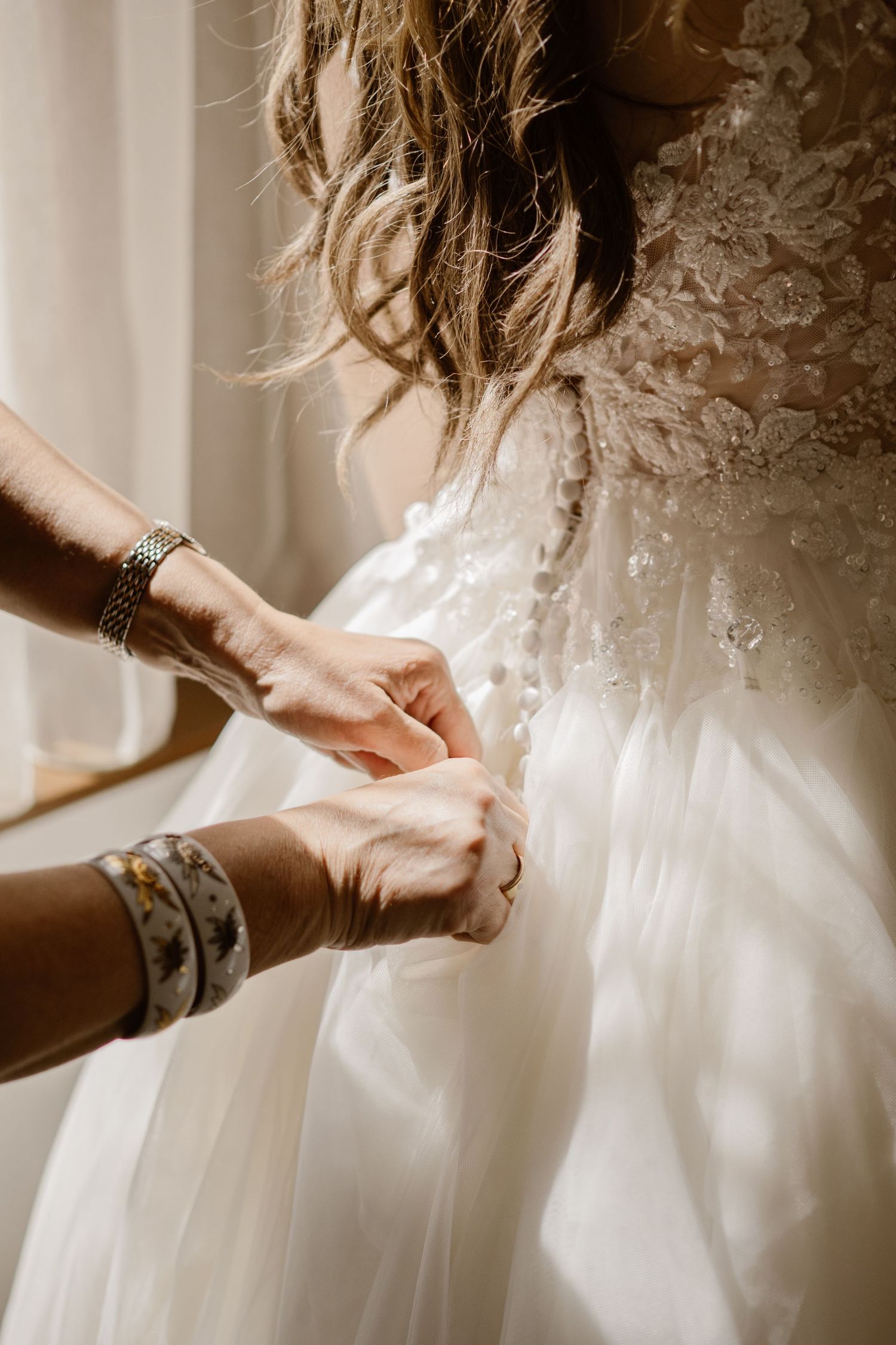 Close-up details of a white lace wedding dress being adjusted and styled.