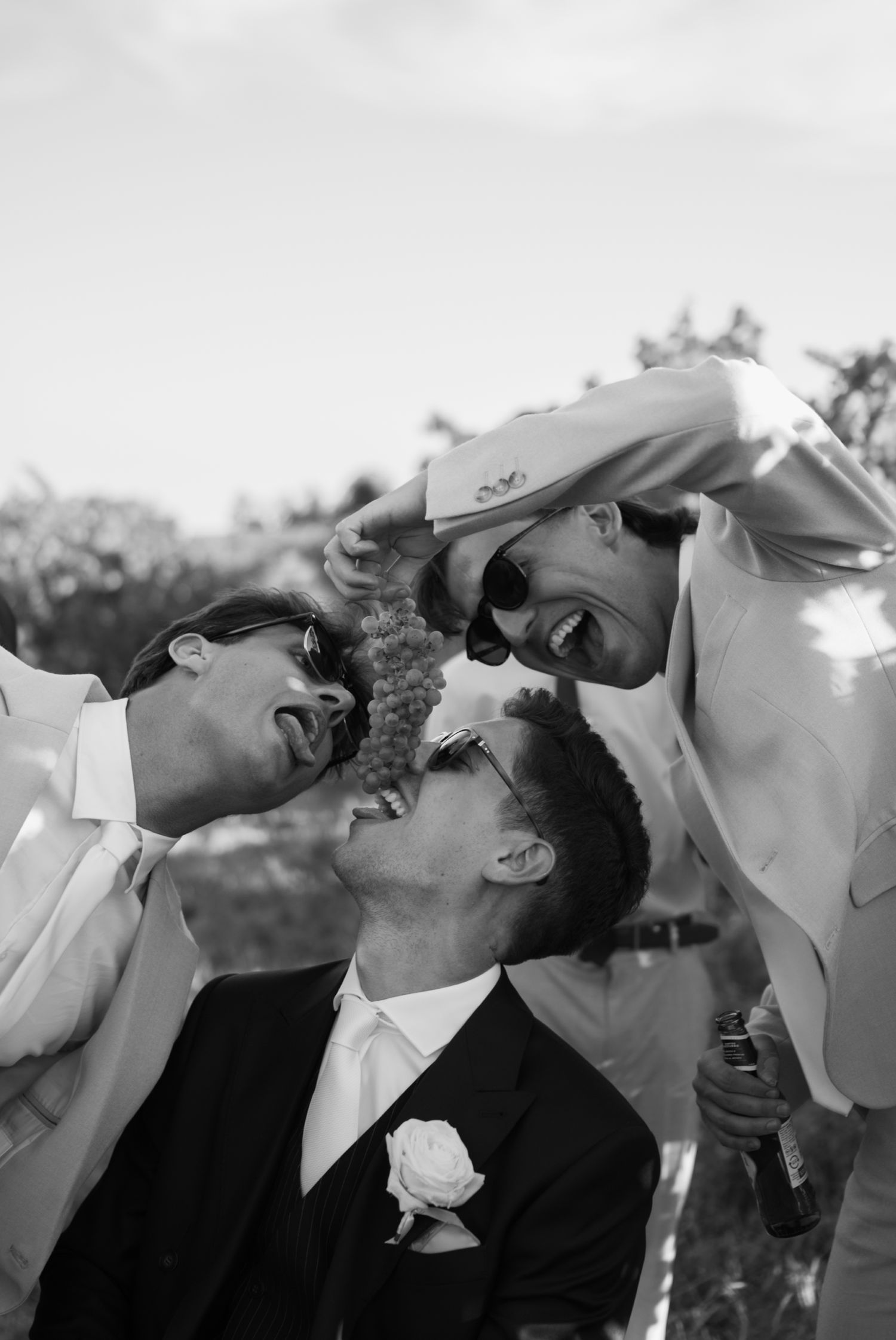 Groom in black suit laughing with groomsmen in black and white wedding photo.