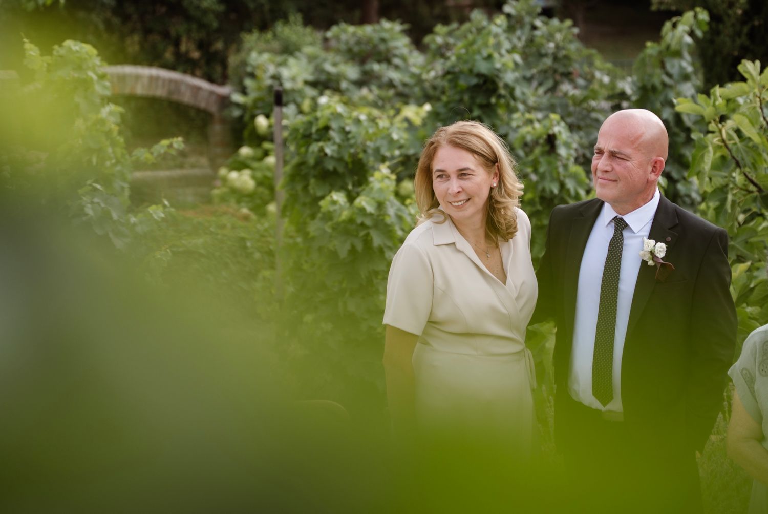 Elegant couple walks through lush garden greenery at a summer wedding celebration.