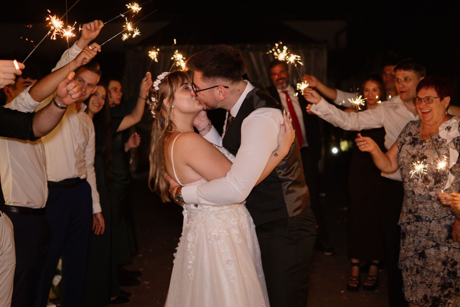Wedding guests dancing with sparklers at an outdoor nighttime celebration.