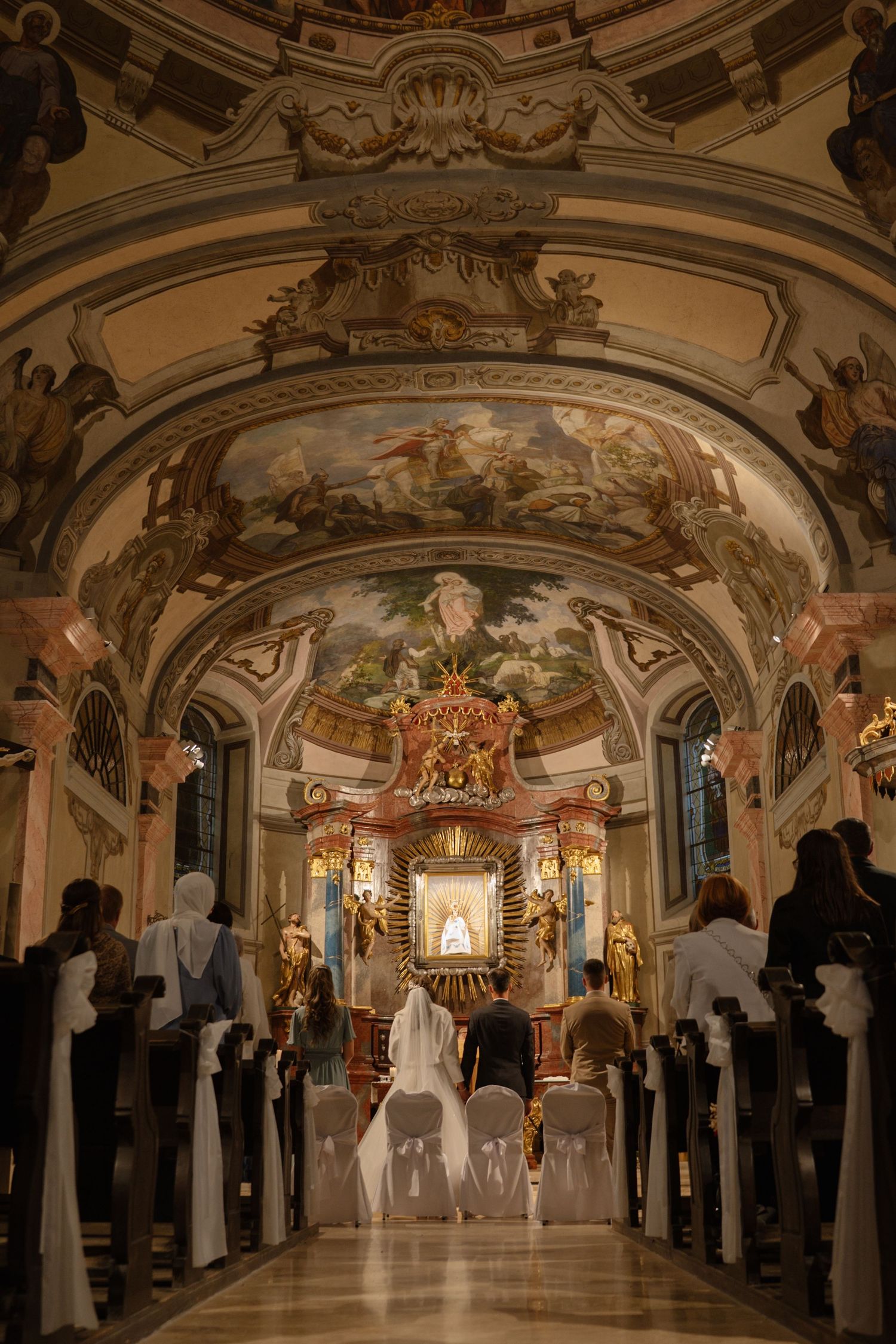 Baroque church interior with painted ceiling frescoes and ornate gold details during a wedding ceremony.