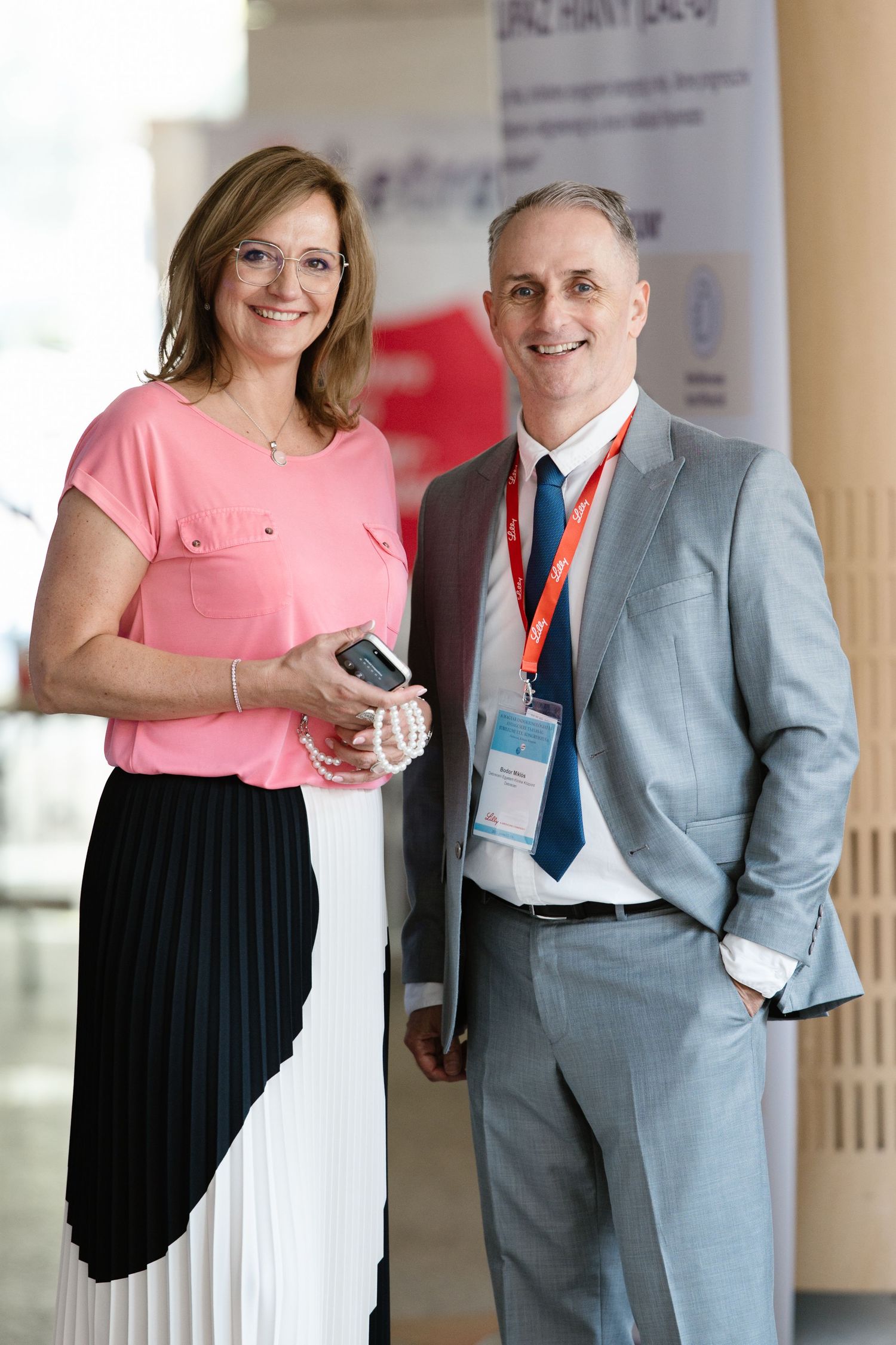 Two people in business attire having a conversation in a professional setting, one wearing pink and one in gray suit.
