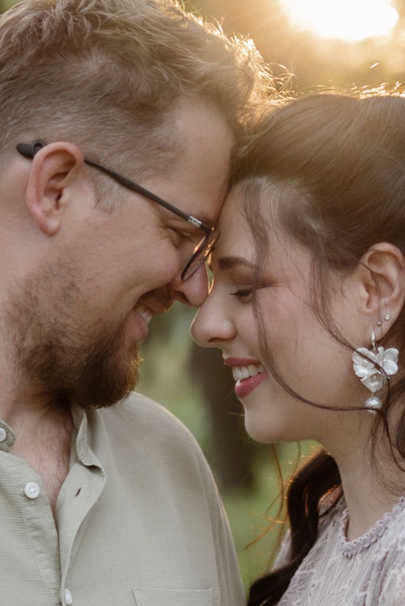A smiling couple touching foreheads in a romantic golden hour outdoor portrait, woman wearing floral earrings.