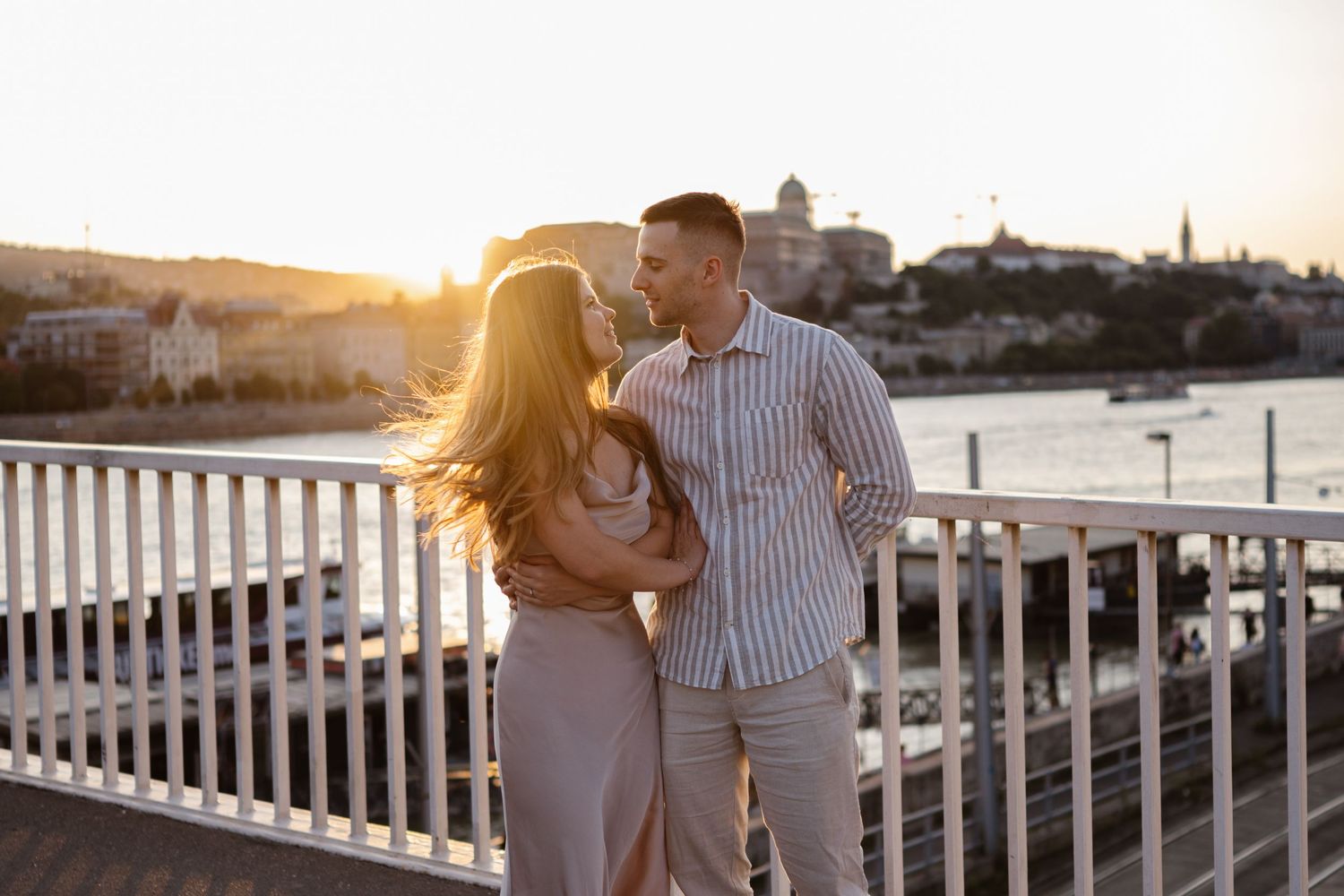 Romantic couple embracing on pier during sunset with harbor view.