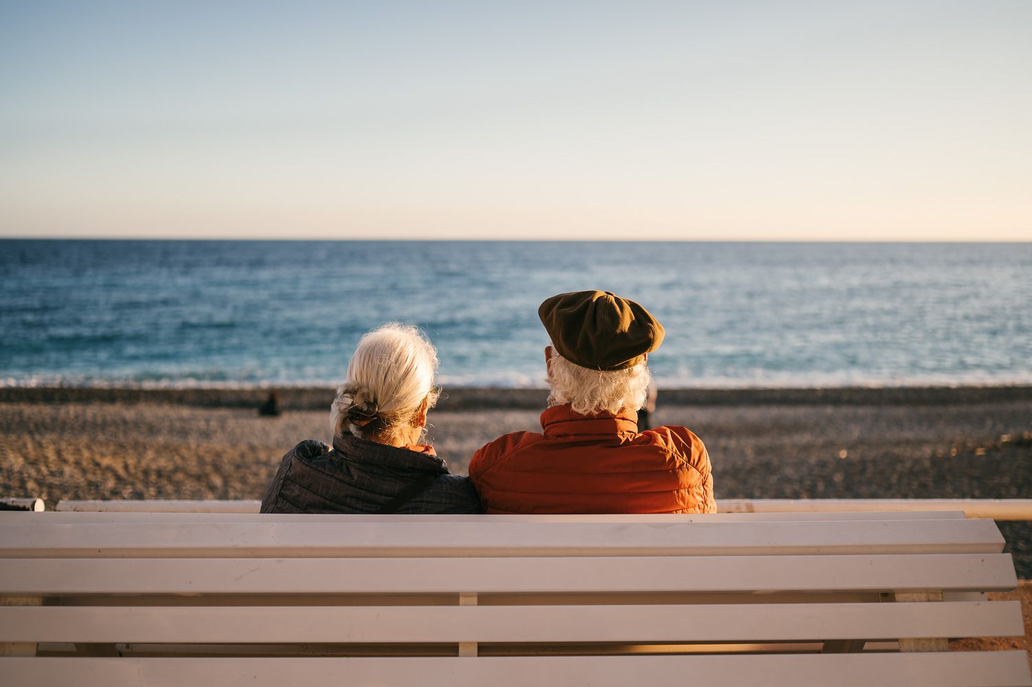 People sitting on a white bench overlooking the ocean at sunset.