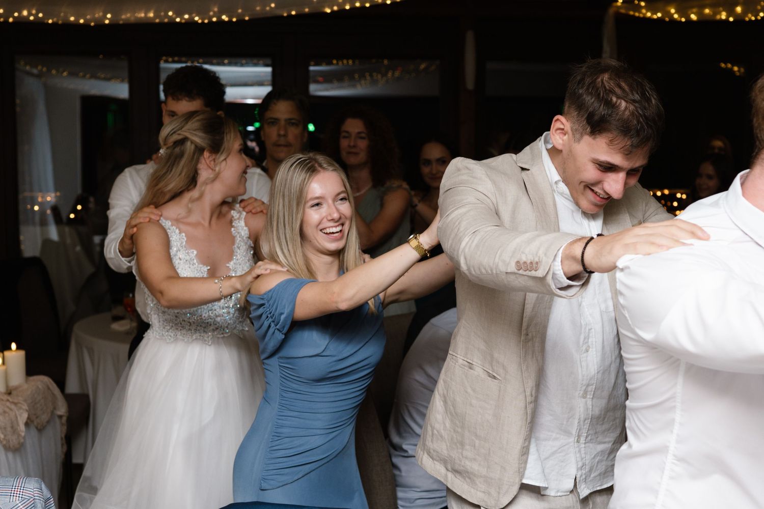 Wedding guests dancing and celebrating at indoor reception with string lights.