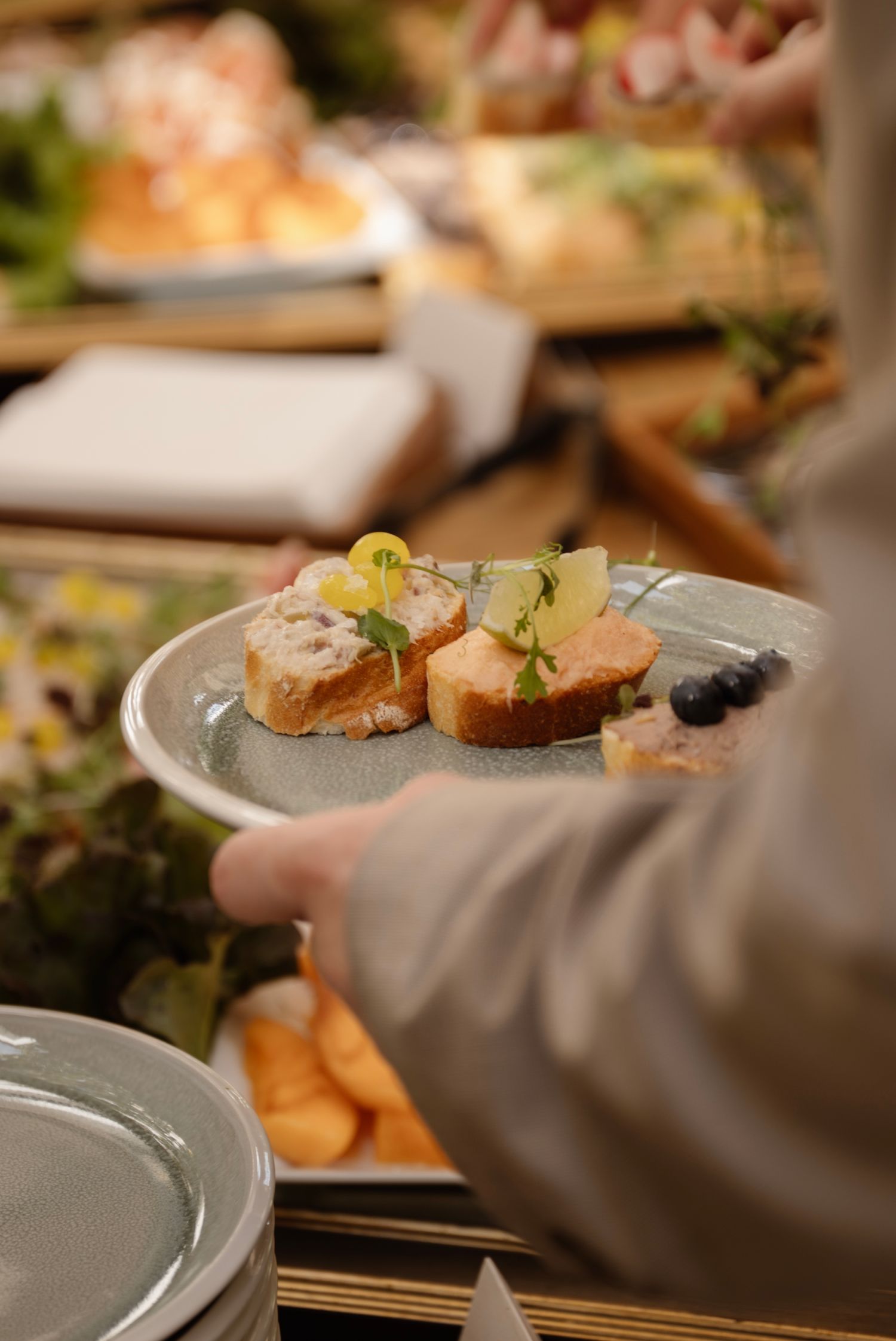 A server holds a plate of elegant bruschetta topped with pate and fresh herbs at a wedding reception buffet.