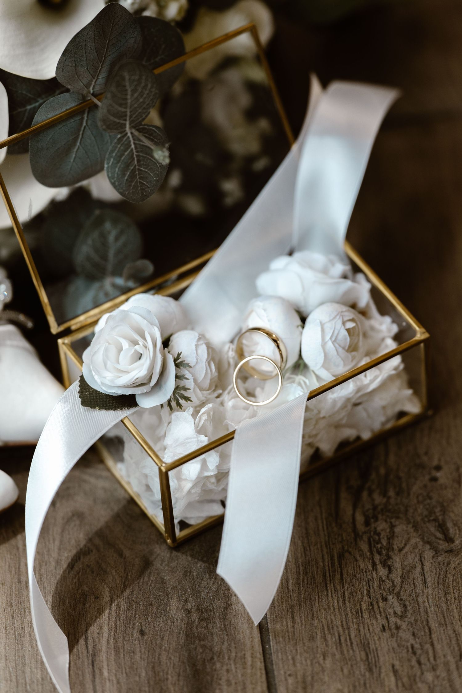 White paper roses with gold stems arranged in a line on rustic wooden surface create an elegant display.