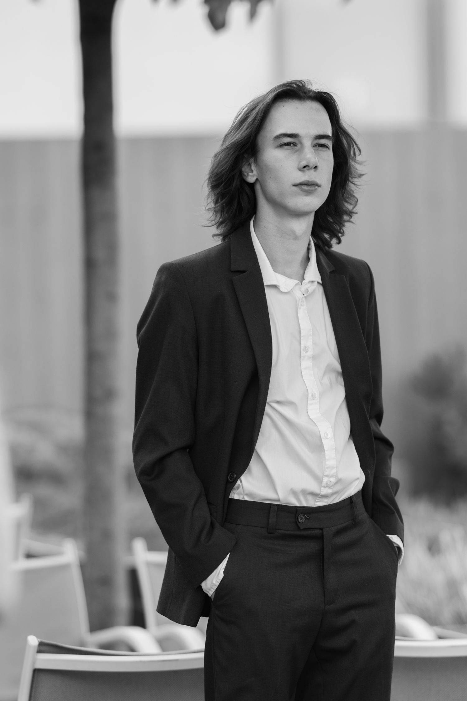 A black and white portrait of someone in a dark suit and white shirt with shoulder-length hair.