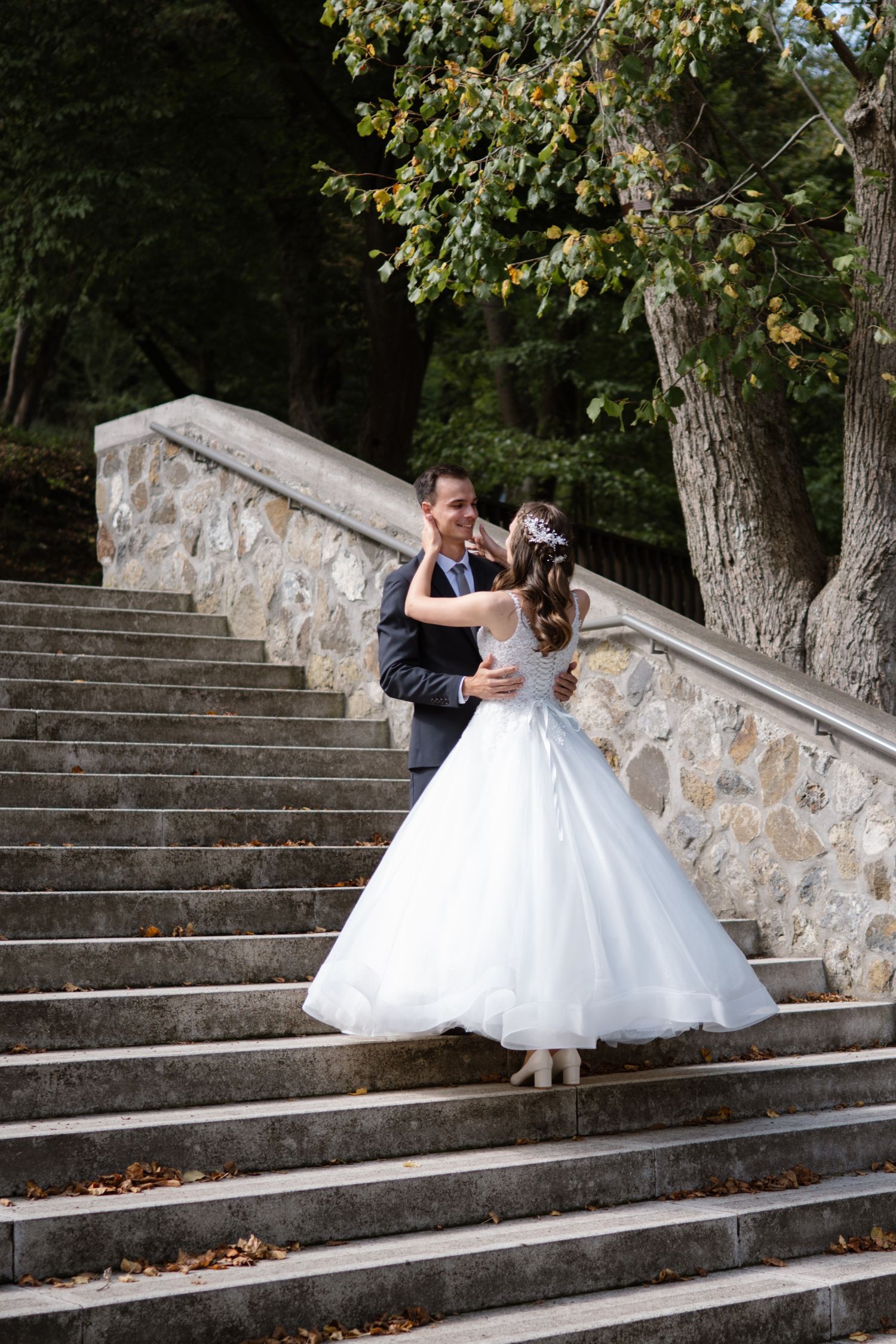 A couple dances on stone steps surrounded by autumn trees and fallen leaves.