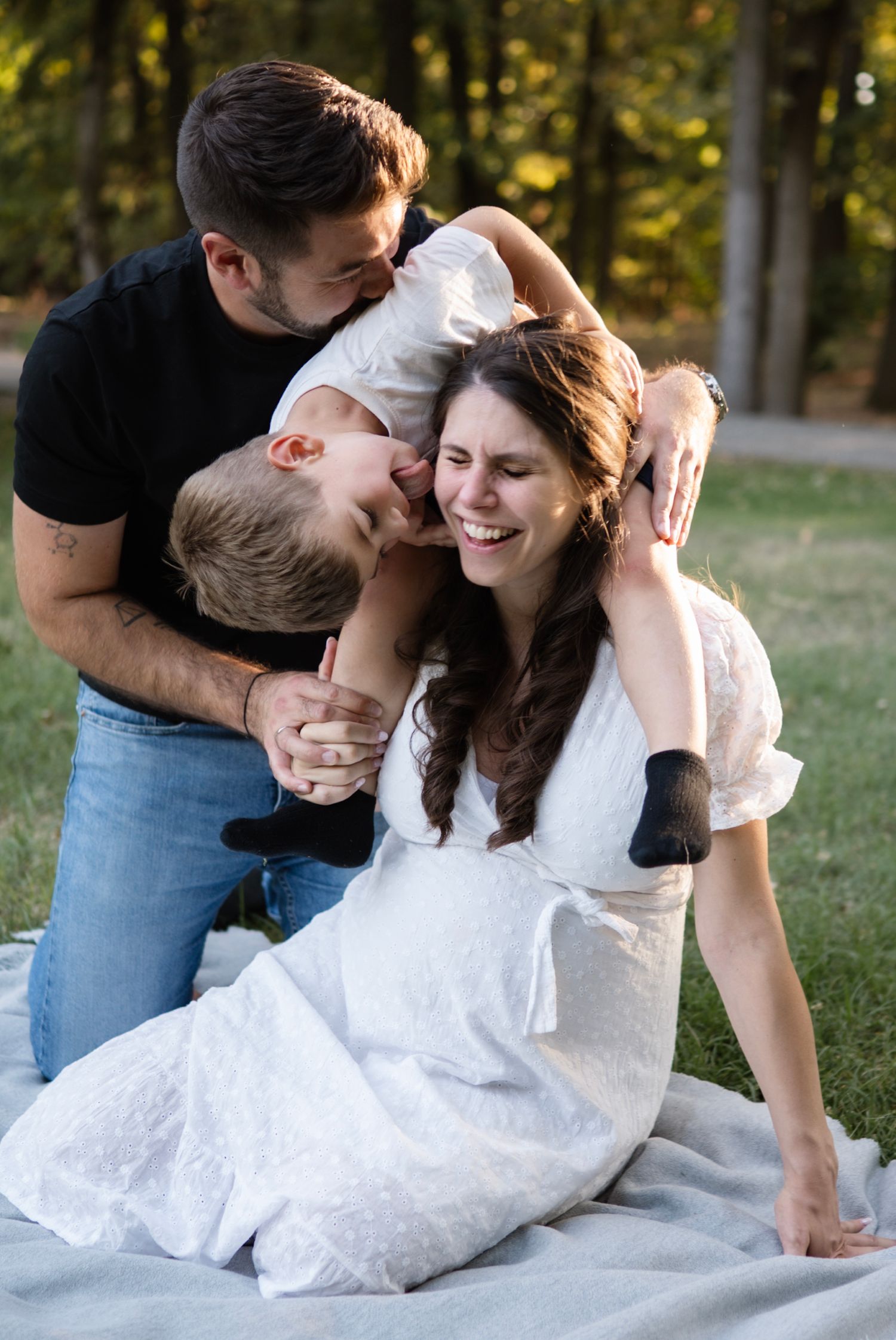 A happy family of three sharing a joyful moment on a blanket in a park, with parents embracing their child.