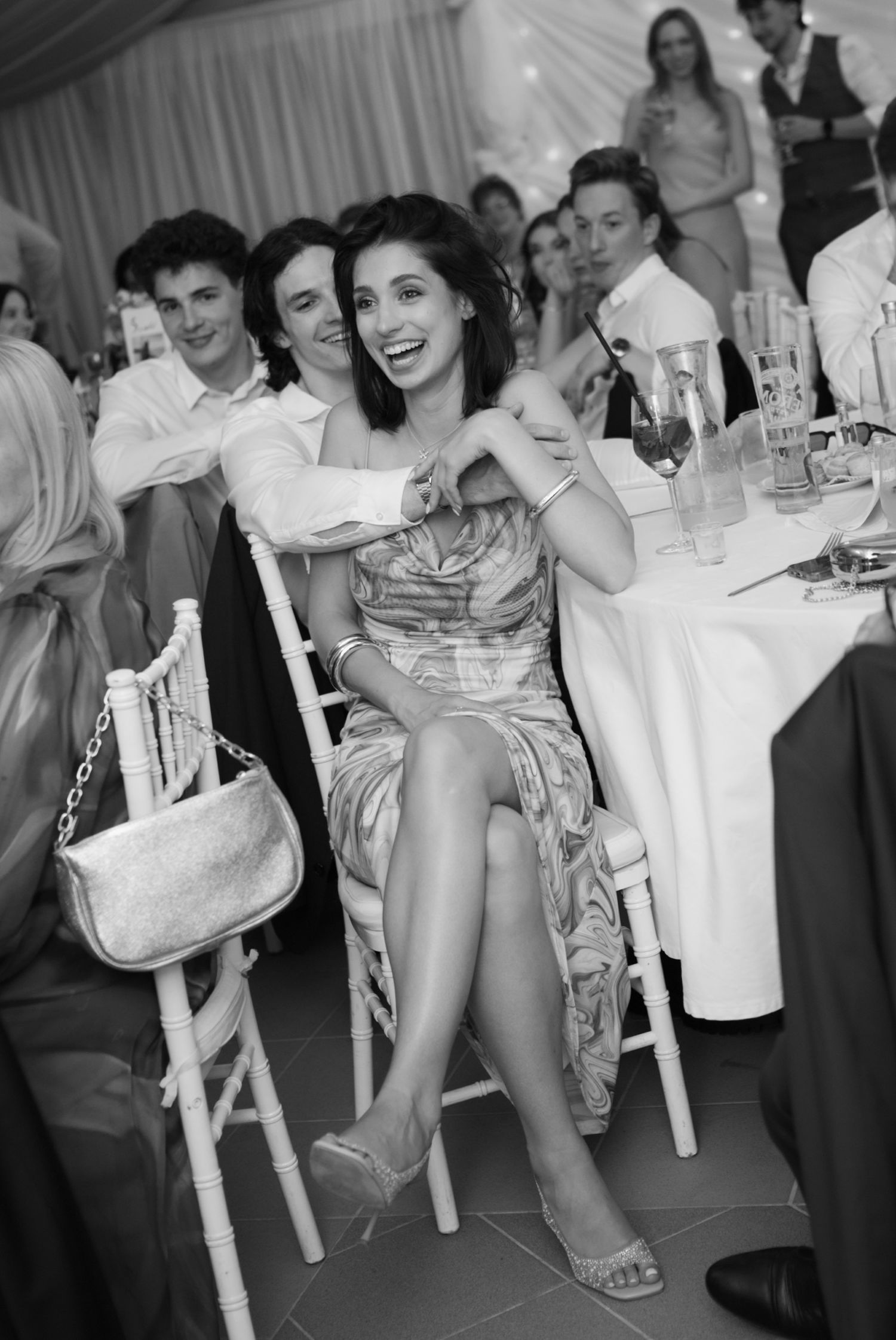Elegant woman in a strapless dress laughing at a wedding reception table in black and white photo.