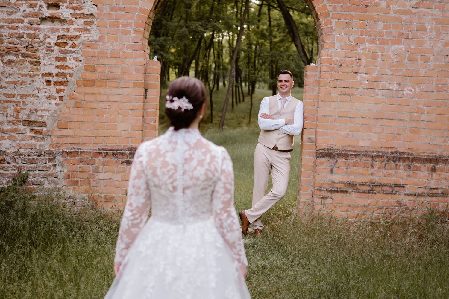 Wedding couple poses against rustic brick wall backdrop outdoors.