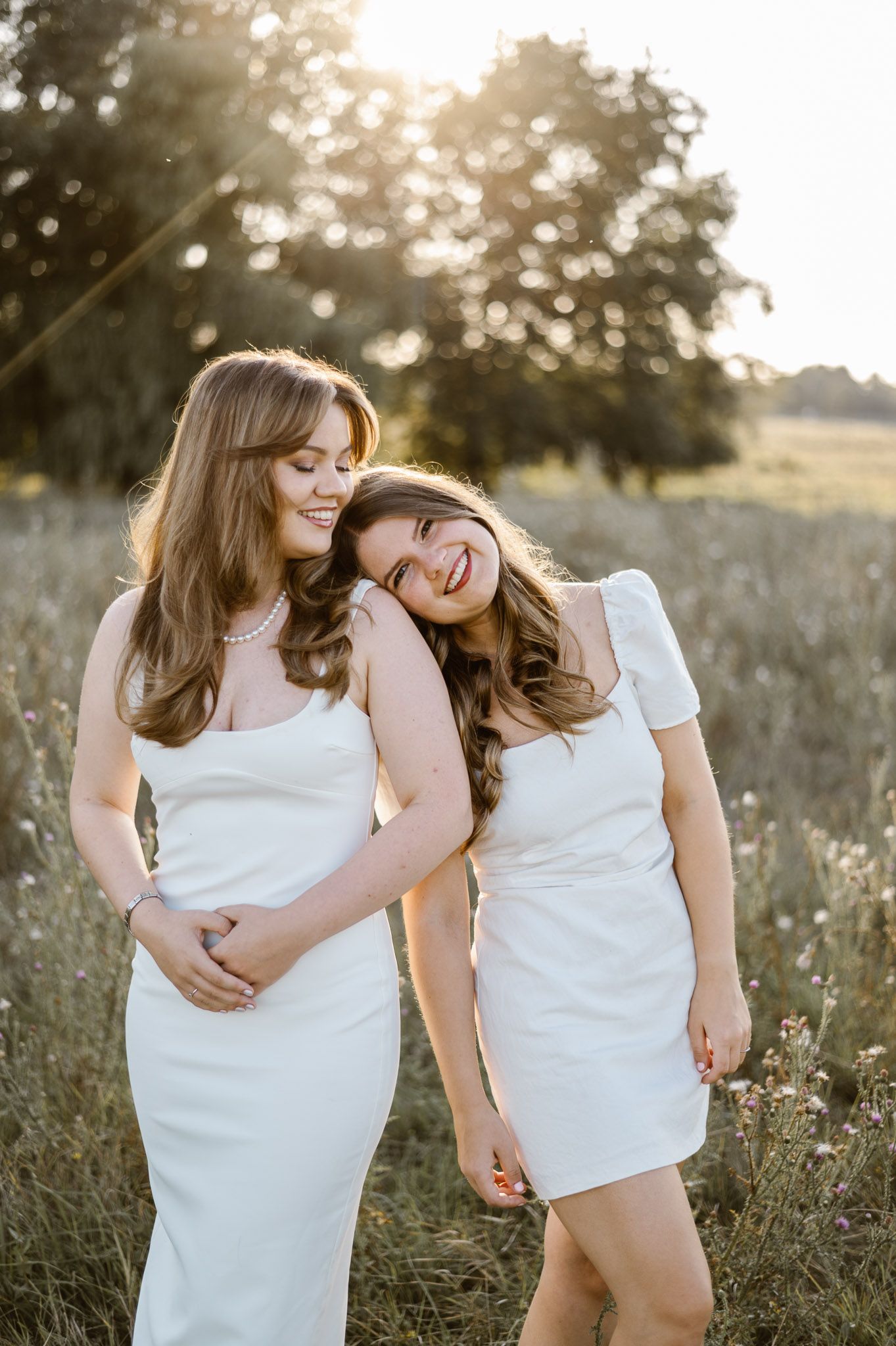 Two people in white dresses sharing tender moments at sunset in a wildflower field.