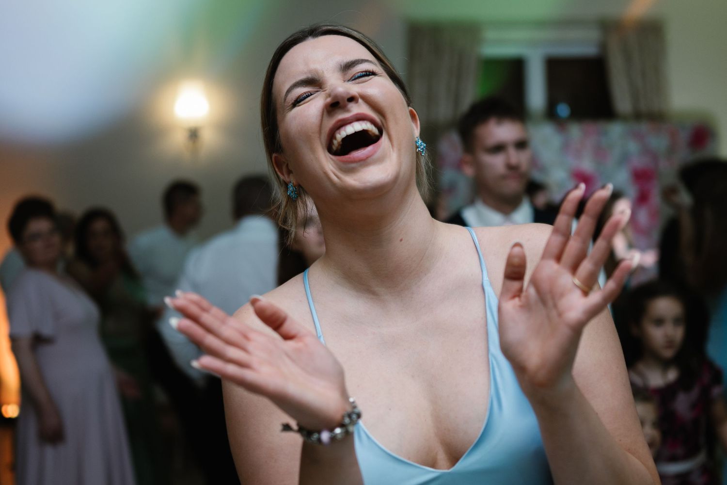Wedding guests laugh and dance during lively reception celebration with ambient lighting.