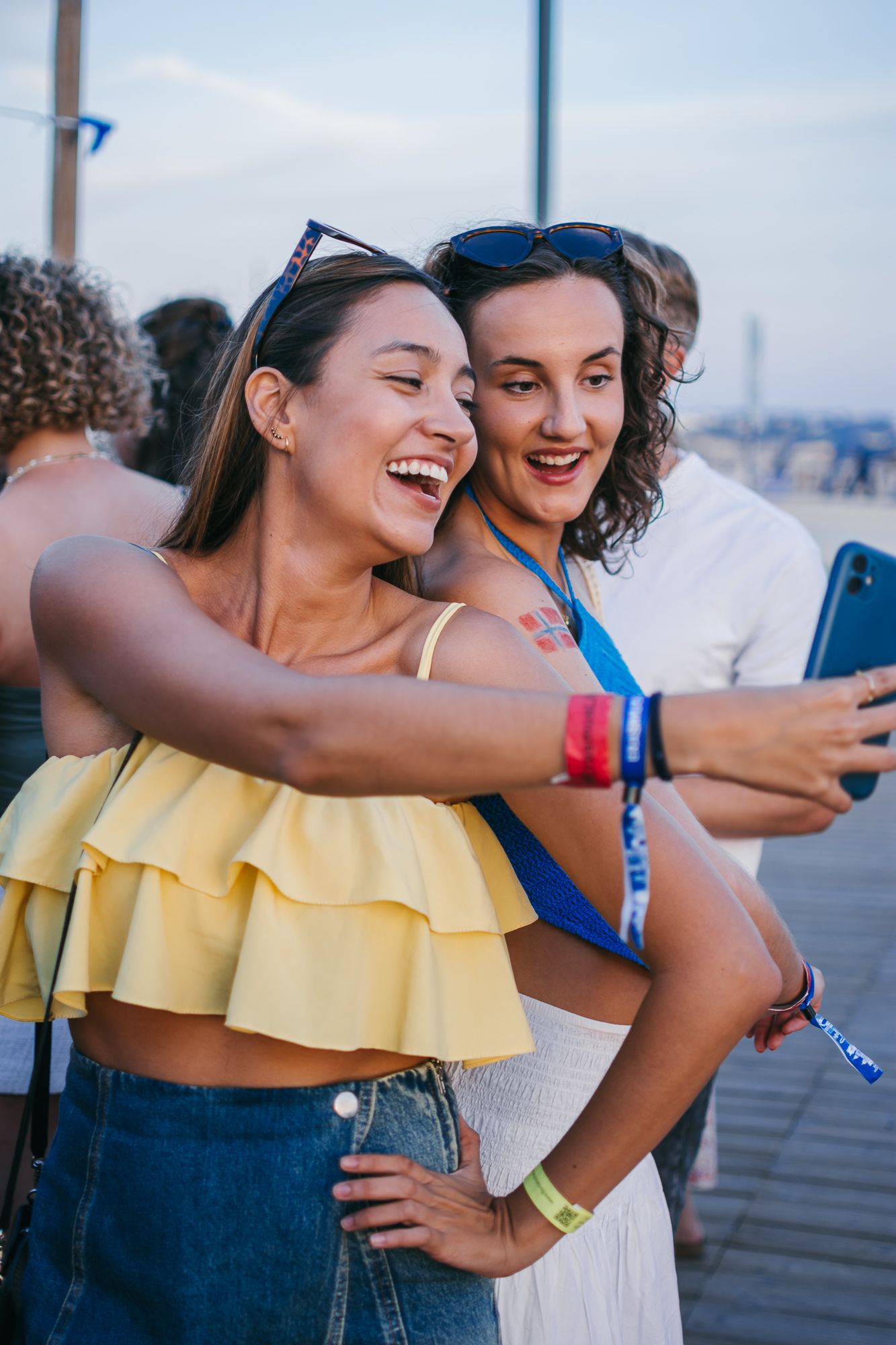 Friends in summer outfits taking selfies on a boardwalk.