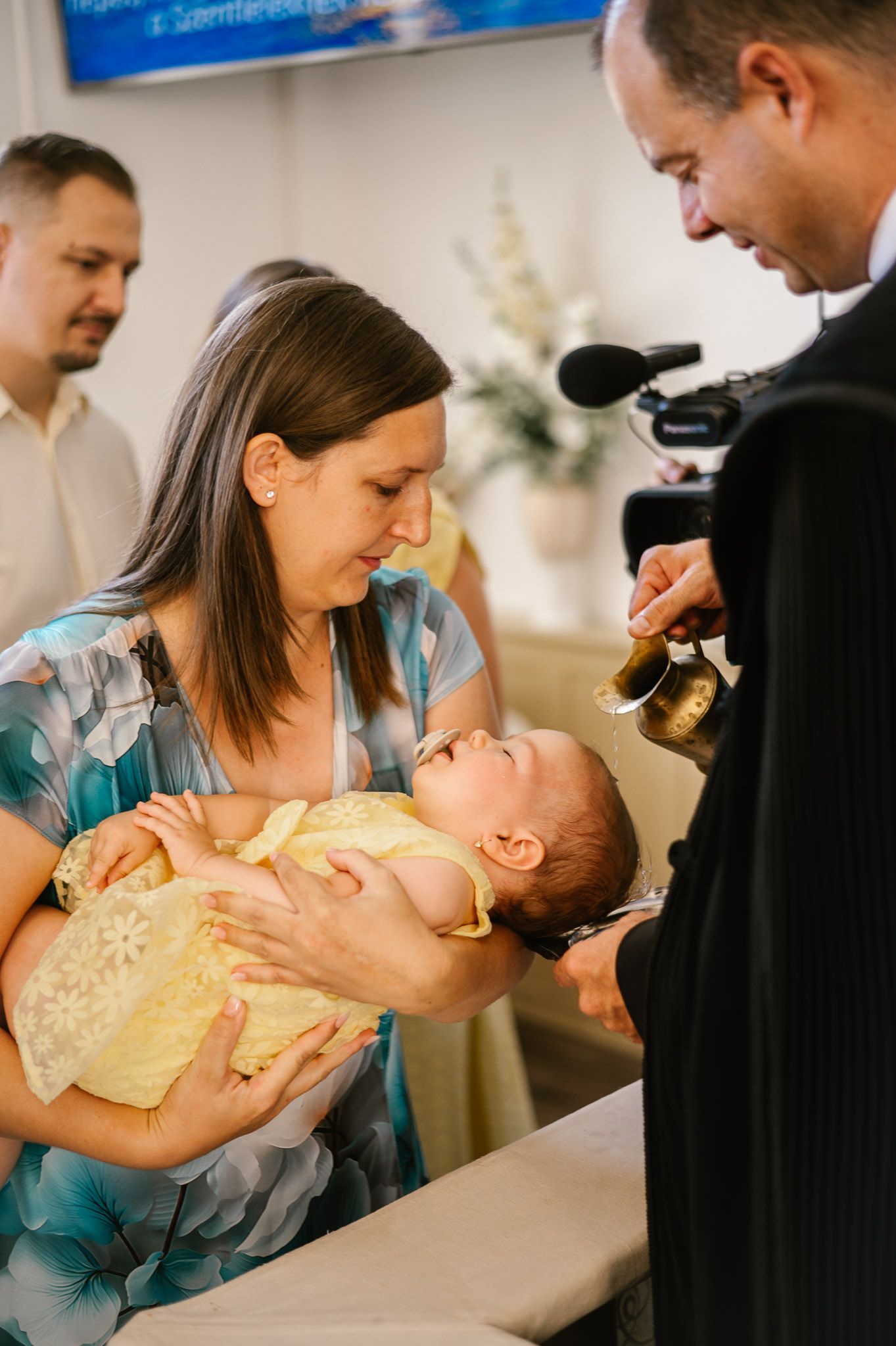 Religious ceremony showing a baby being baptized while held by parents.