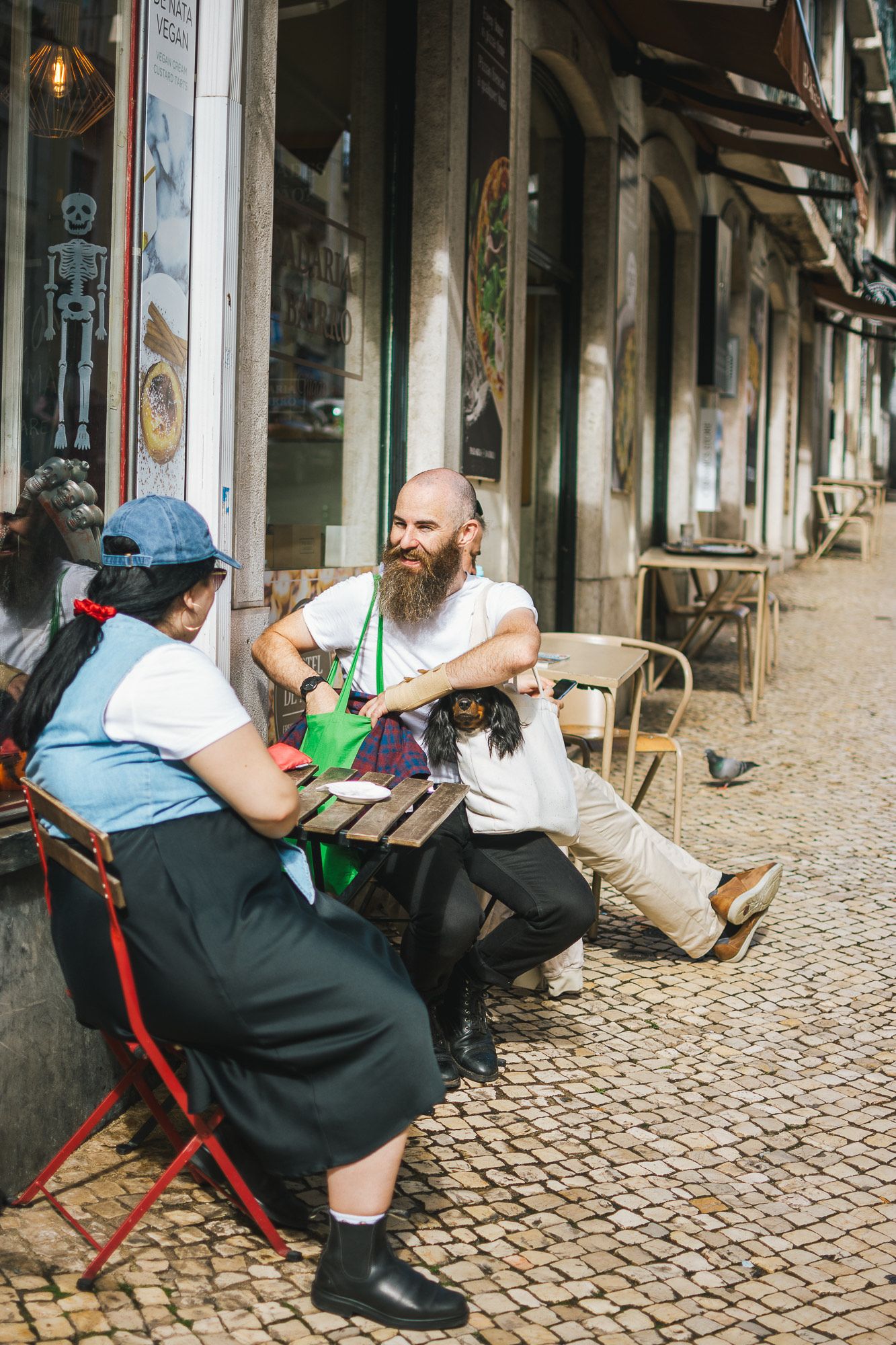 People sitting at outdoor cafe tables on cobblestone street in European city.