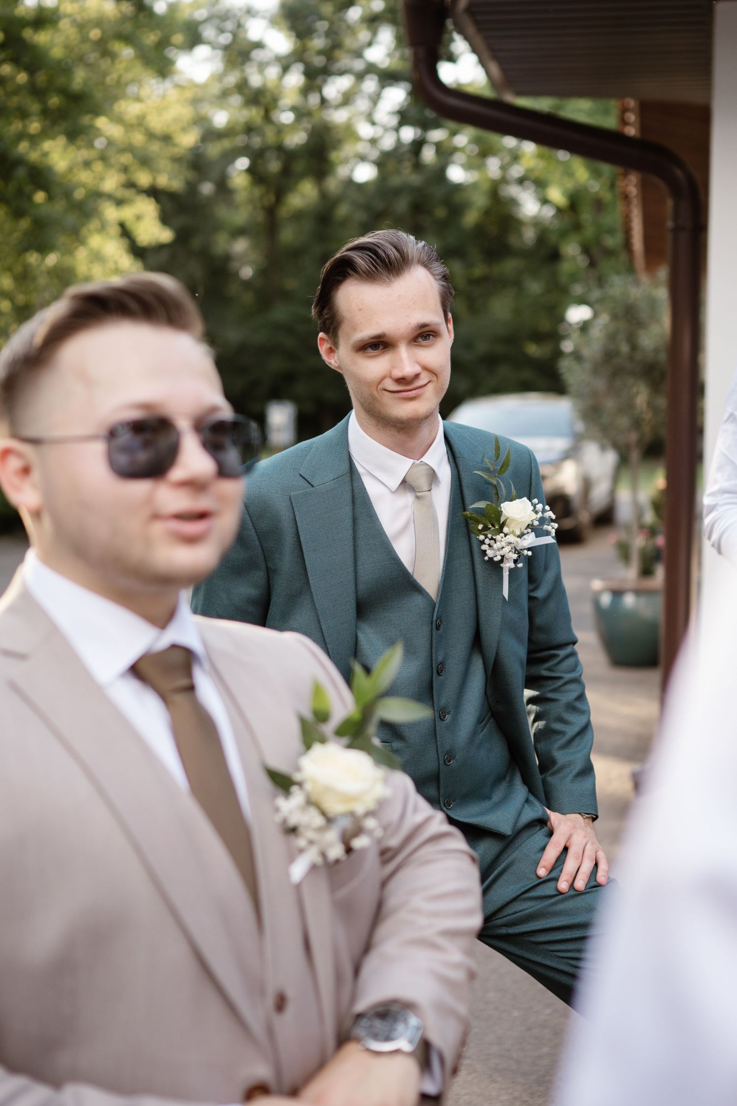 Wedding party in mixed brown and green suits gathered outdoors.