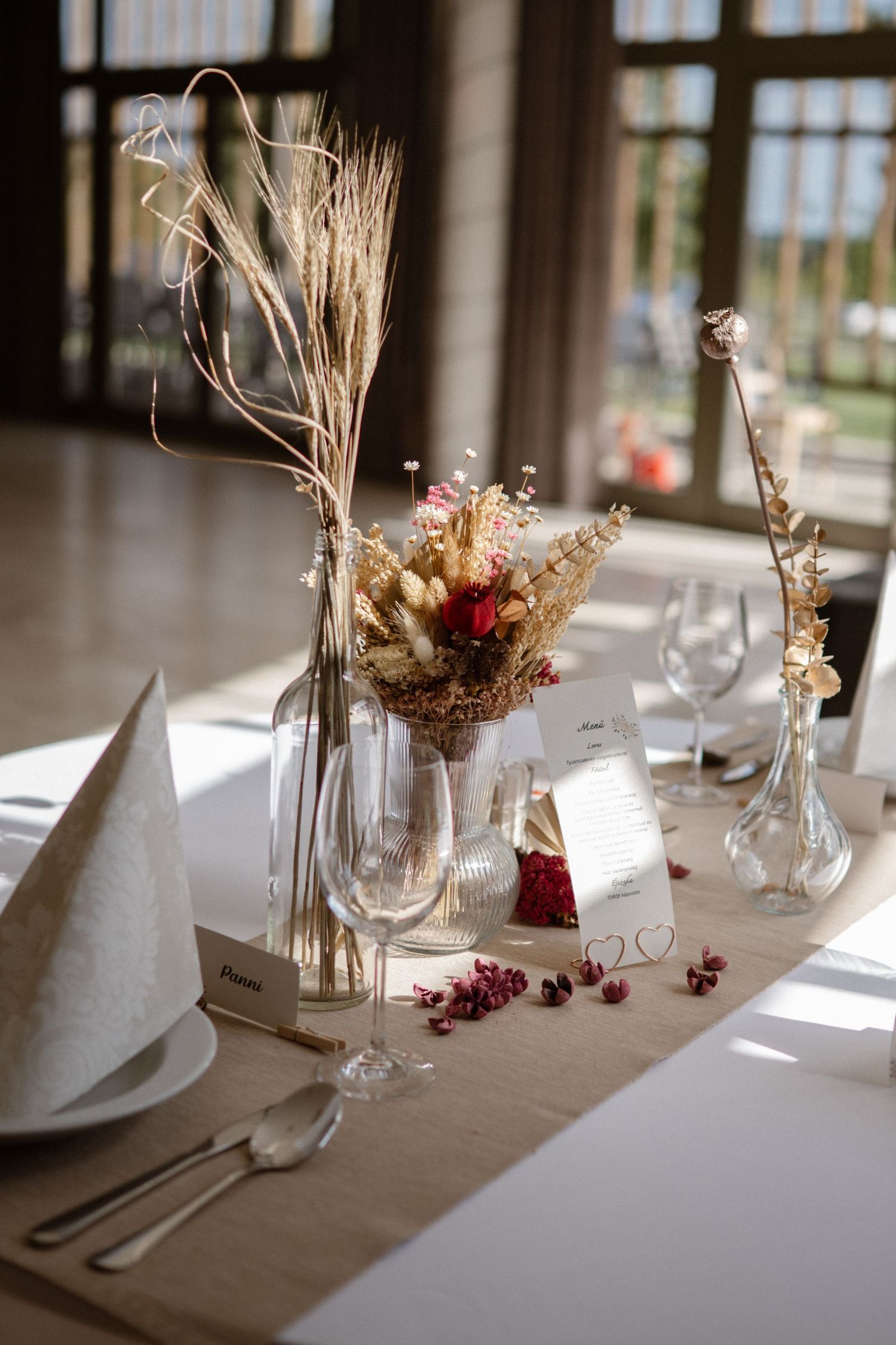 Rustic wedding table decor featuring dried flowers and wheat in glass vases on a linen tablecloth.