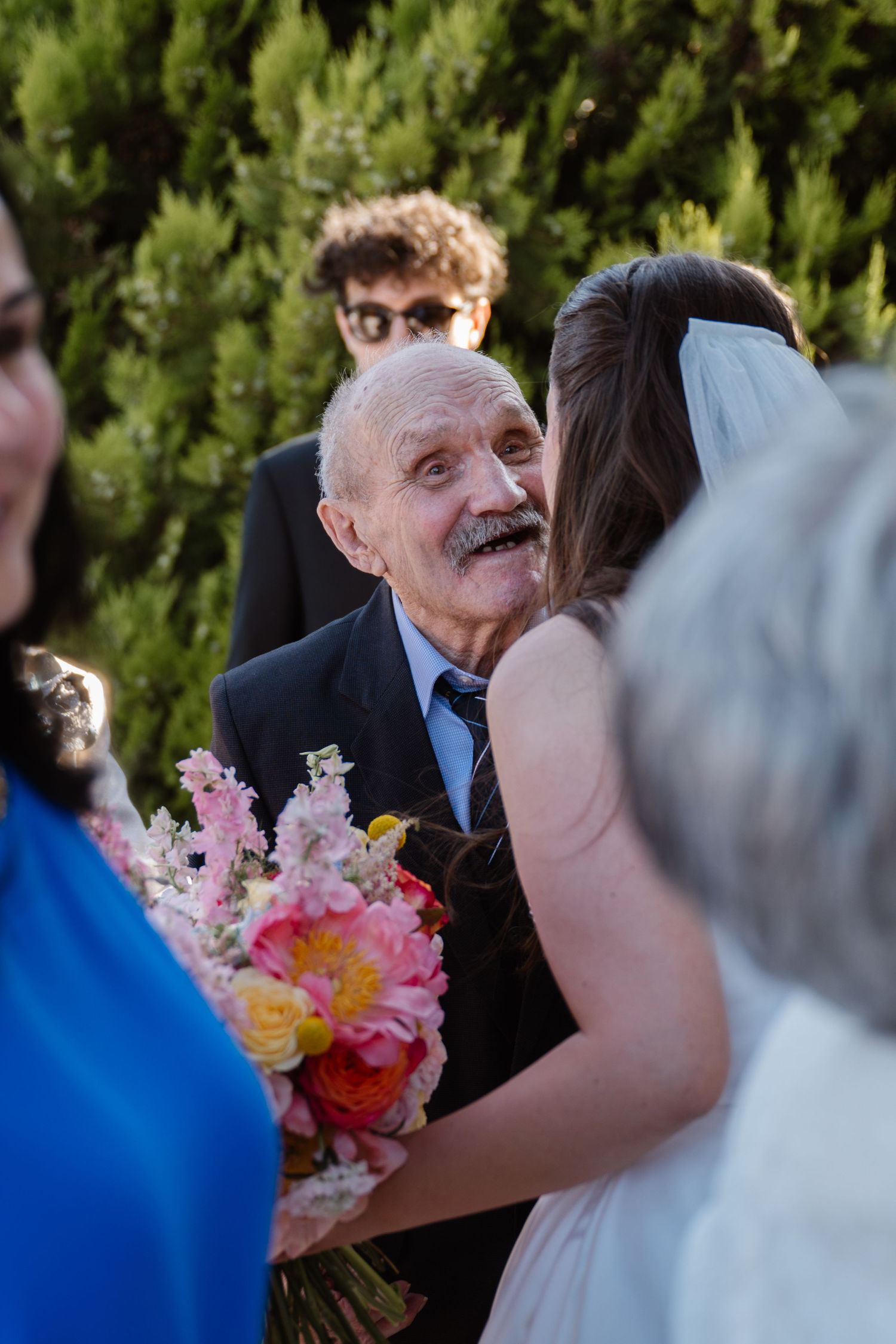 Emotional wedding moment with colorful bouquet and greenery backdrop.
