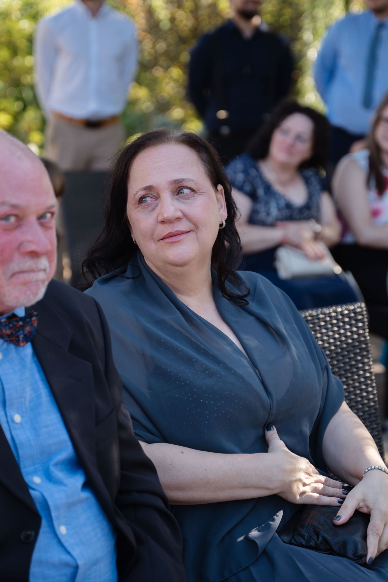 Wedding guests seated outdoors in dark attire watching ceremony.