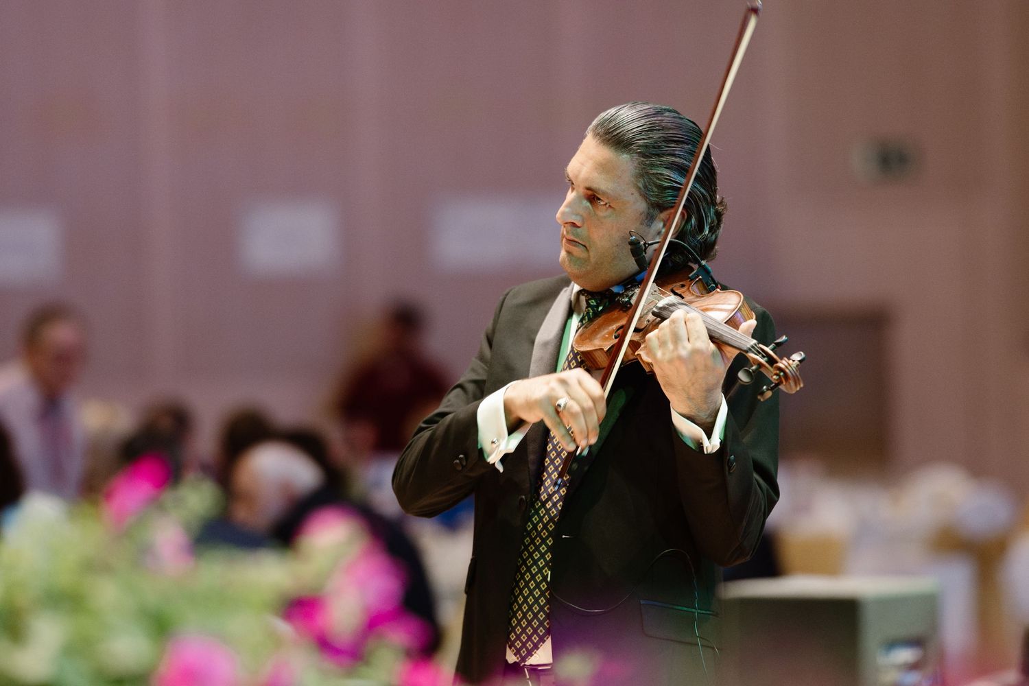 Violinist performing at formal event wearing black suit and tie.